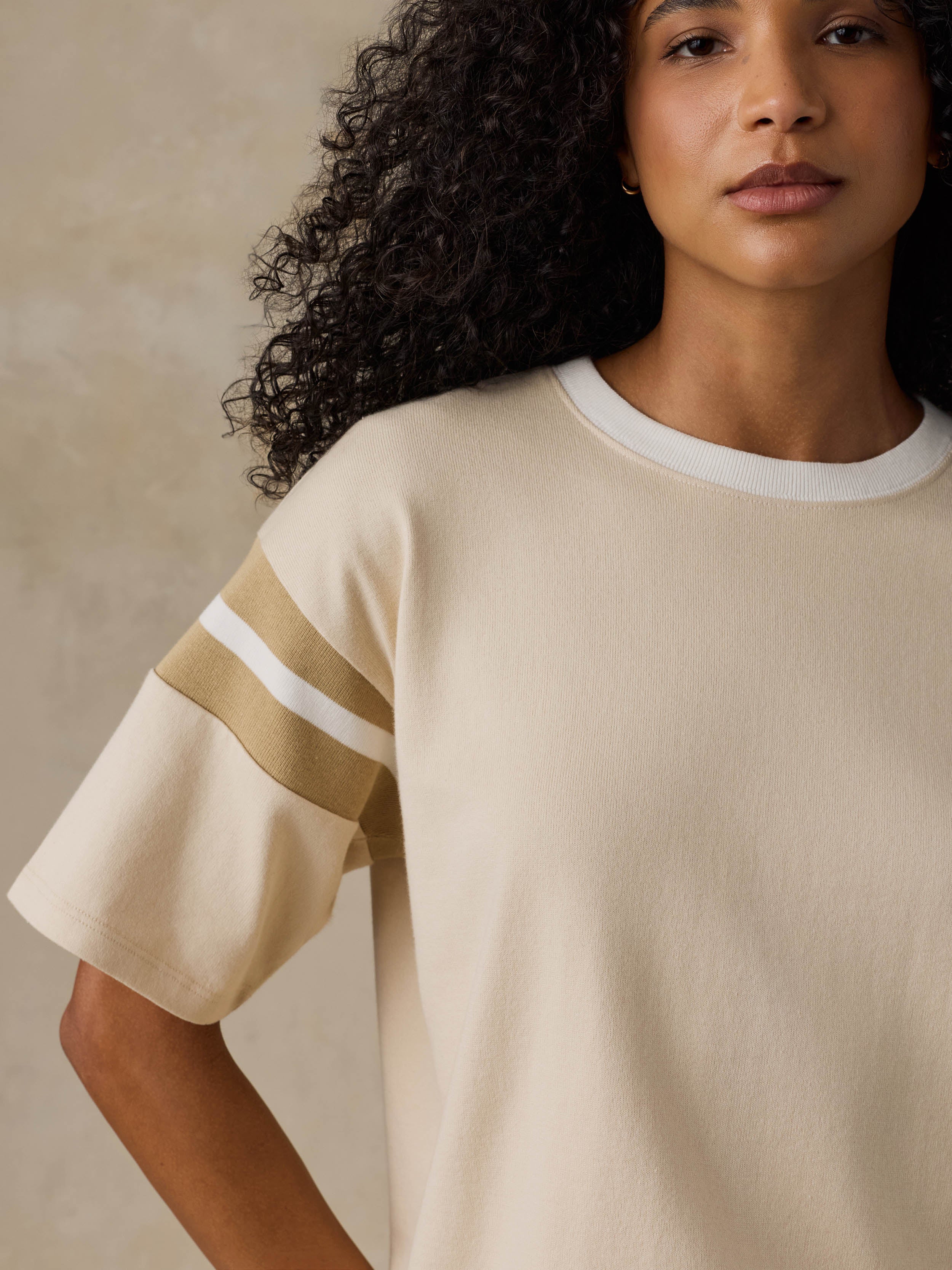 A close-up of a woman wearing a cream-colored short-sleeve knit top with a white crew neck and two diagonal stripes on the sleeve in beige and white.