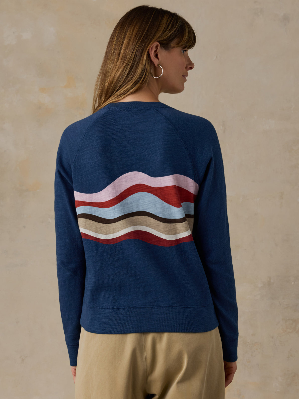 Woman wearing a navy blue and multicolor graphic crewneck with beige chino pants against a beige background, image 3 of 6