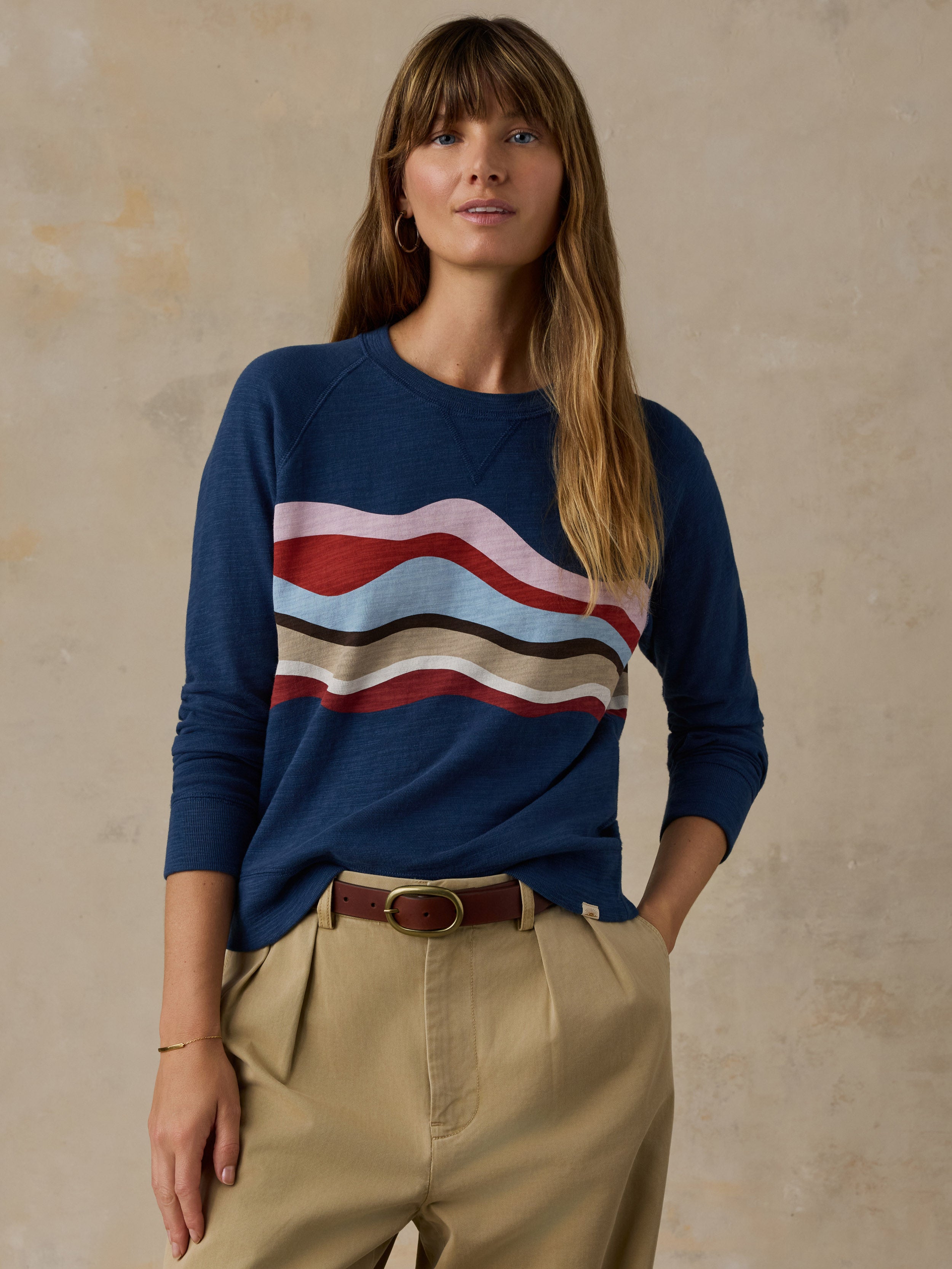 Woman wearing a navy blue and multicolor graphic crewneck with beige chino pants against a beige background