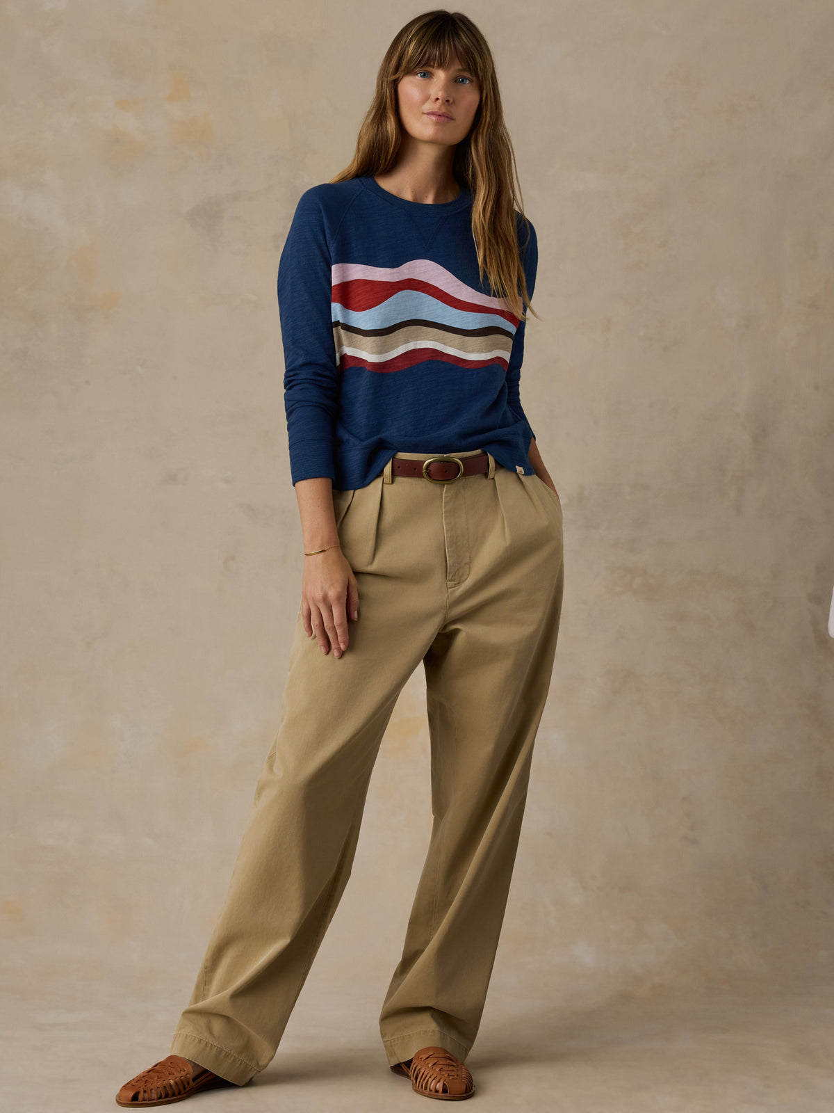 Woman wearing a navy blue and multicolor graphic crewneck with beige chino pants against a beige background, image 5 of 6