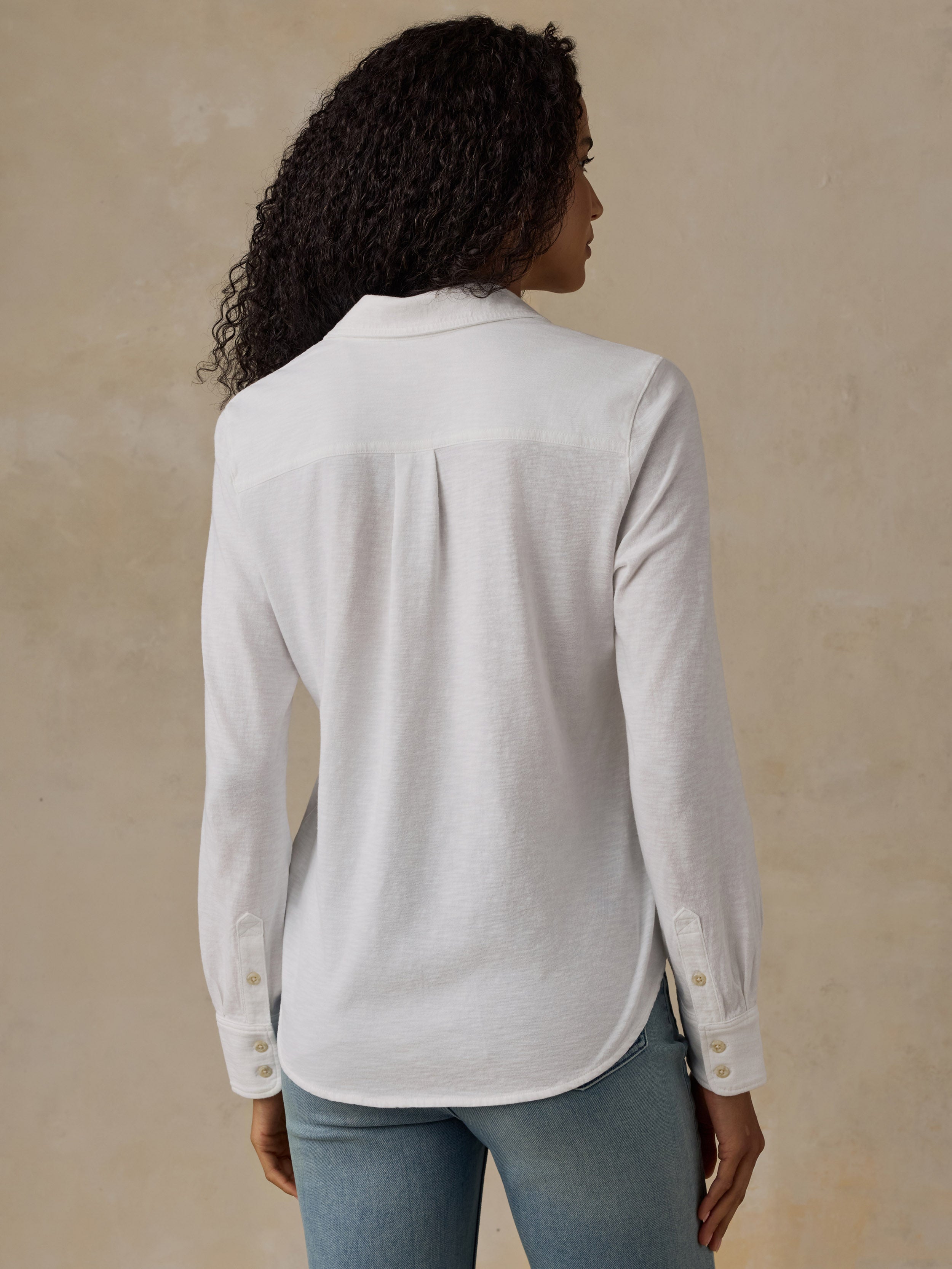 Woman wearing a white button down shirt and blue jeans against a beige background