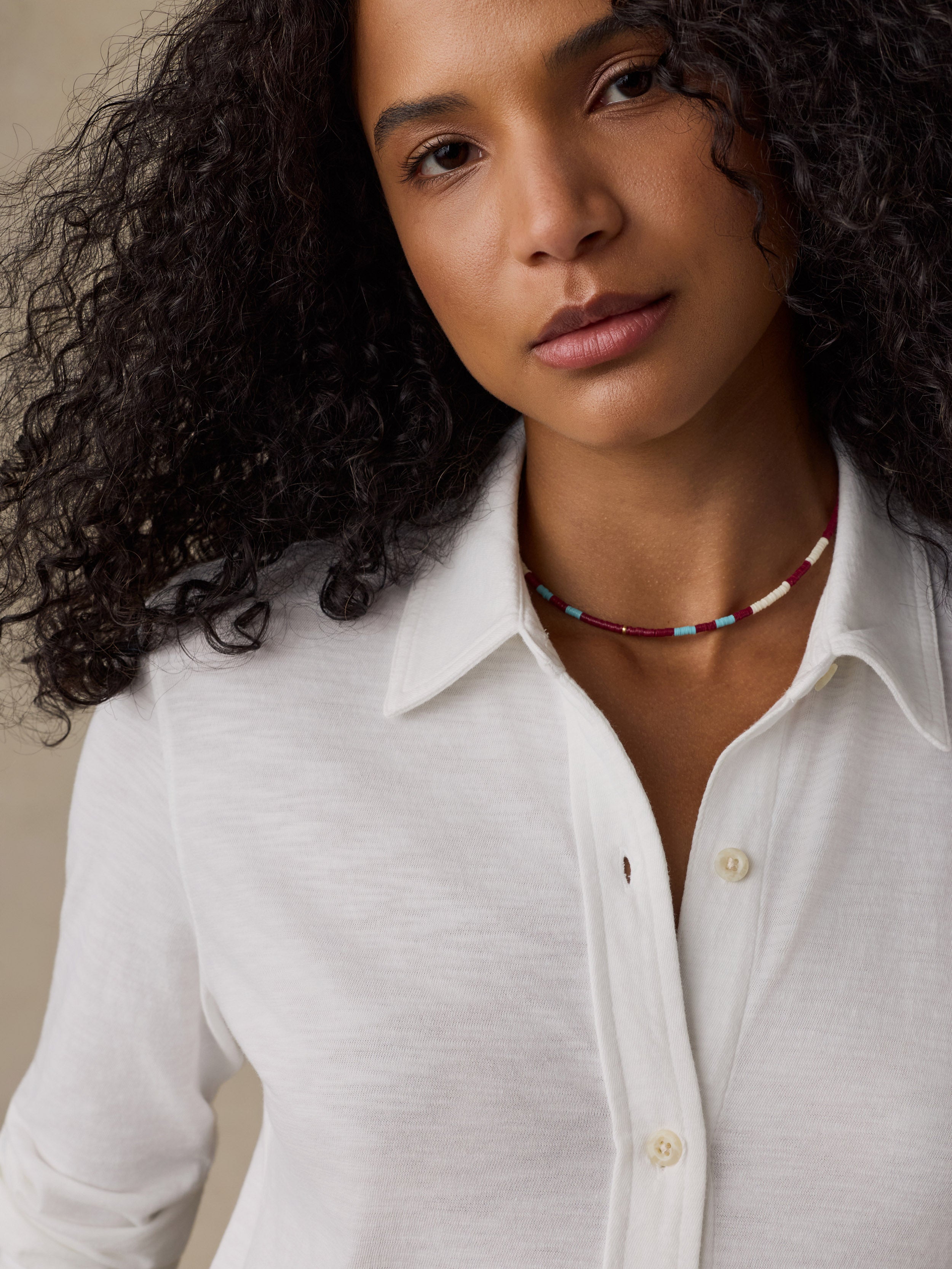 Woman wearing a white button down shirt against a beige background