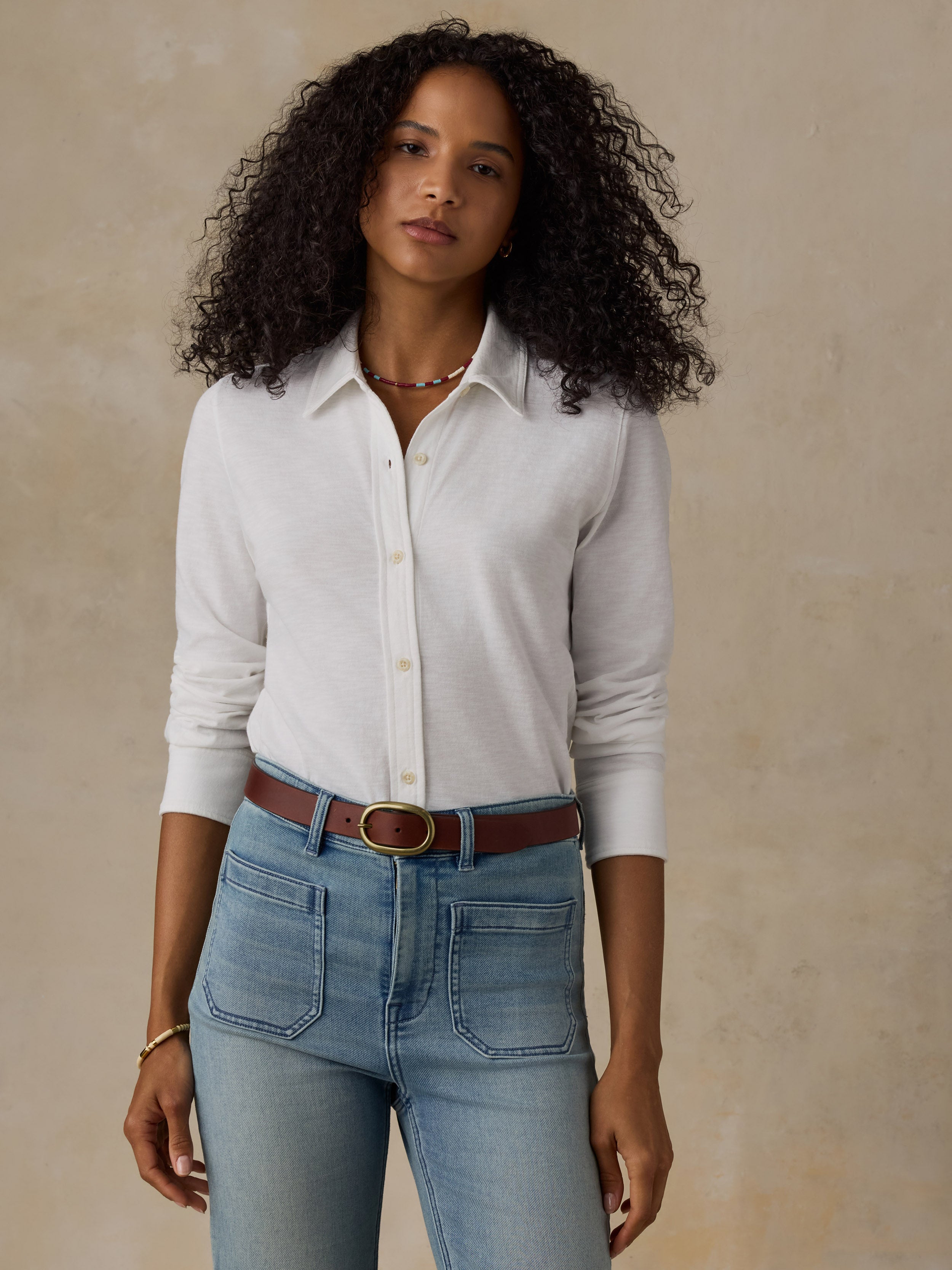 Woman wearing a white button down shirt and blue jeans against a beige background