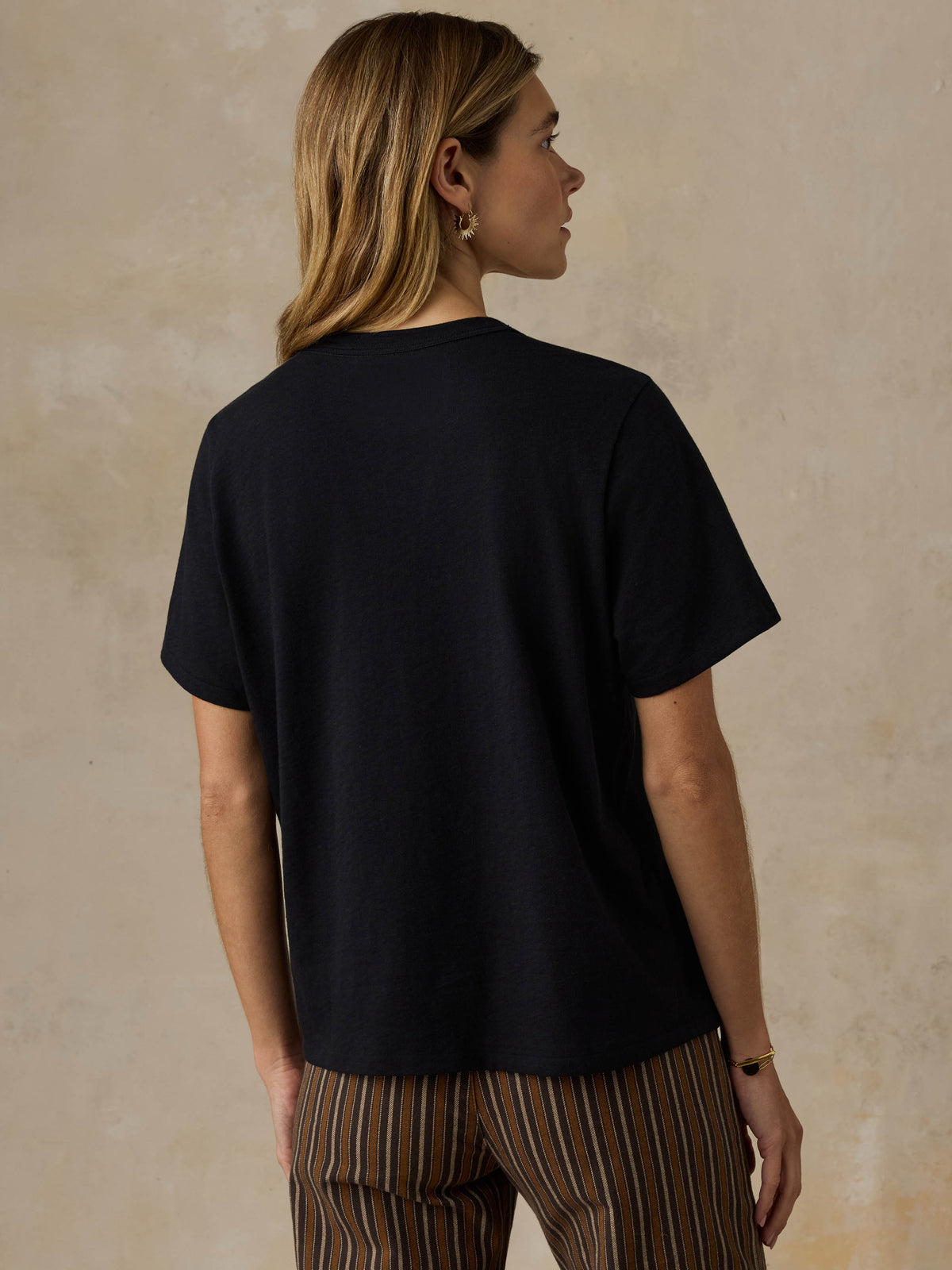 Woman wearing a black t-shirt and striped pants against a beige background, image 4 of 7