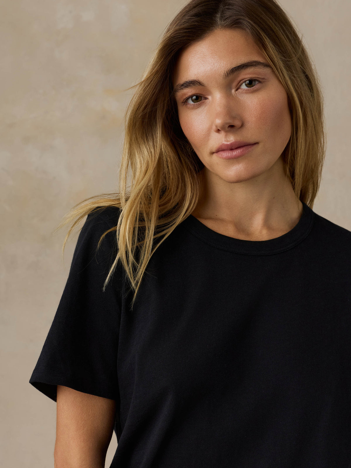 Woman wearing a black t-shirt against a beige background, image 3 of 7