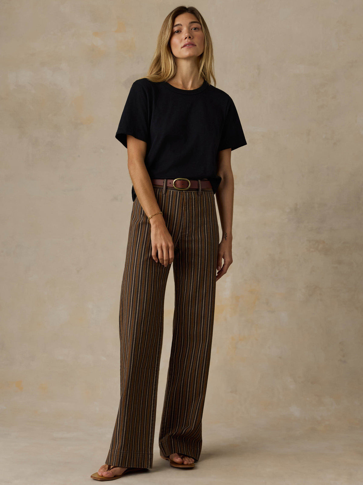 Woman wearing a black t-shirt and striped pants against a beige background, image 5 of 7