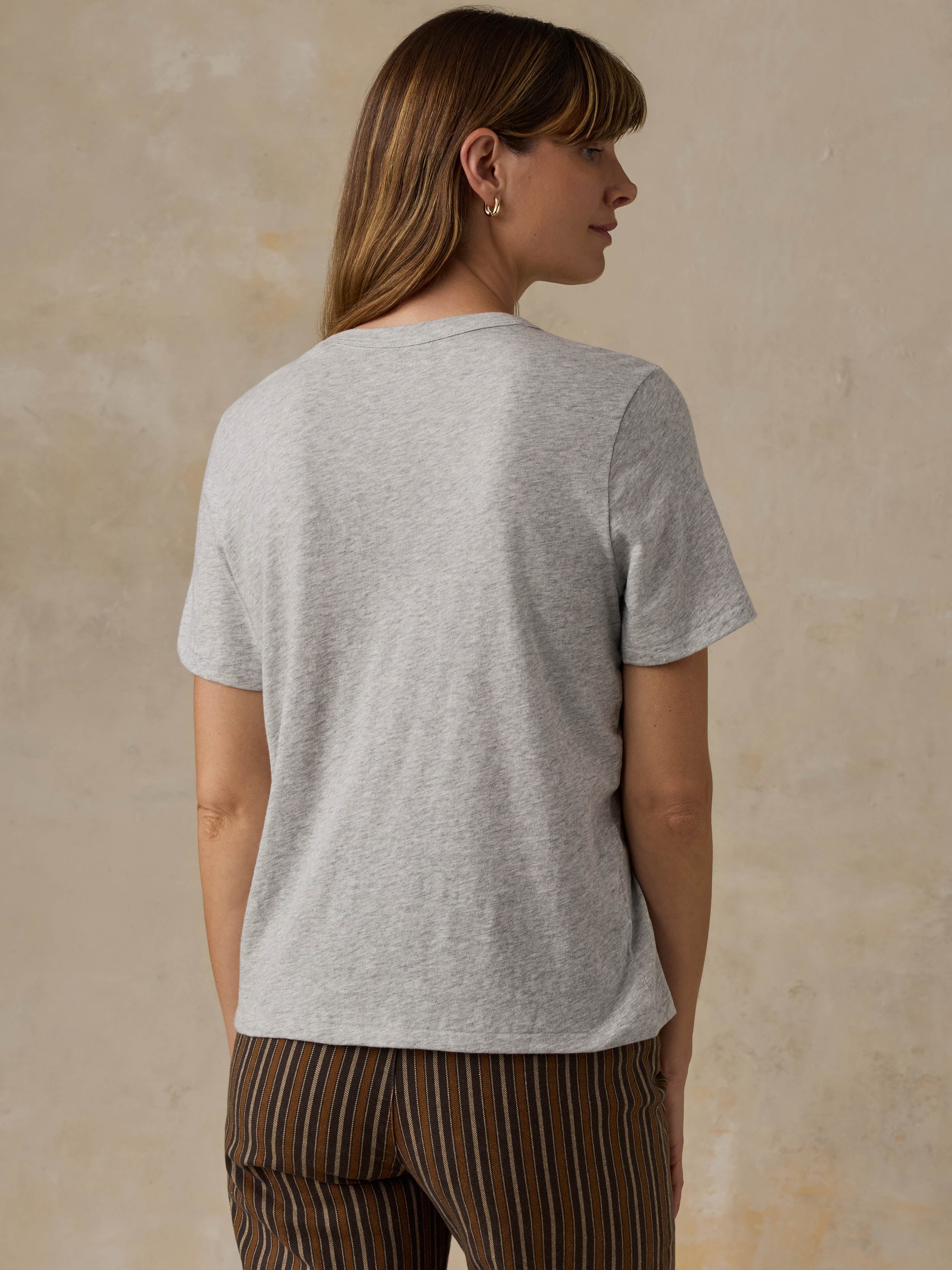A woman wearing a grey t-shirt and striped pants against a beige background