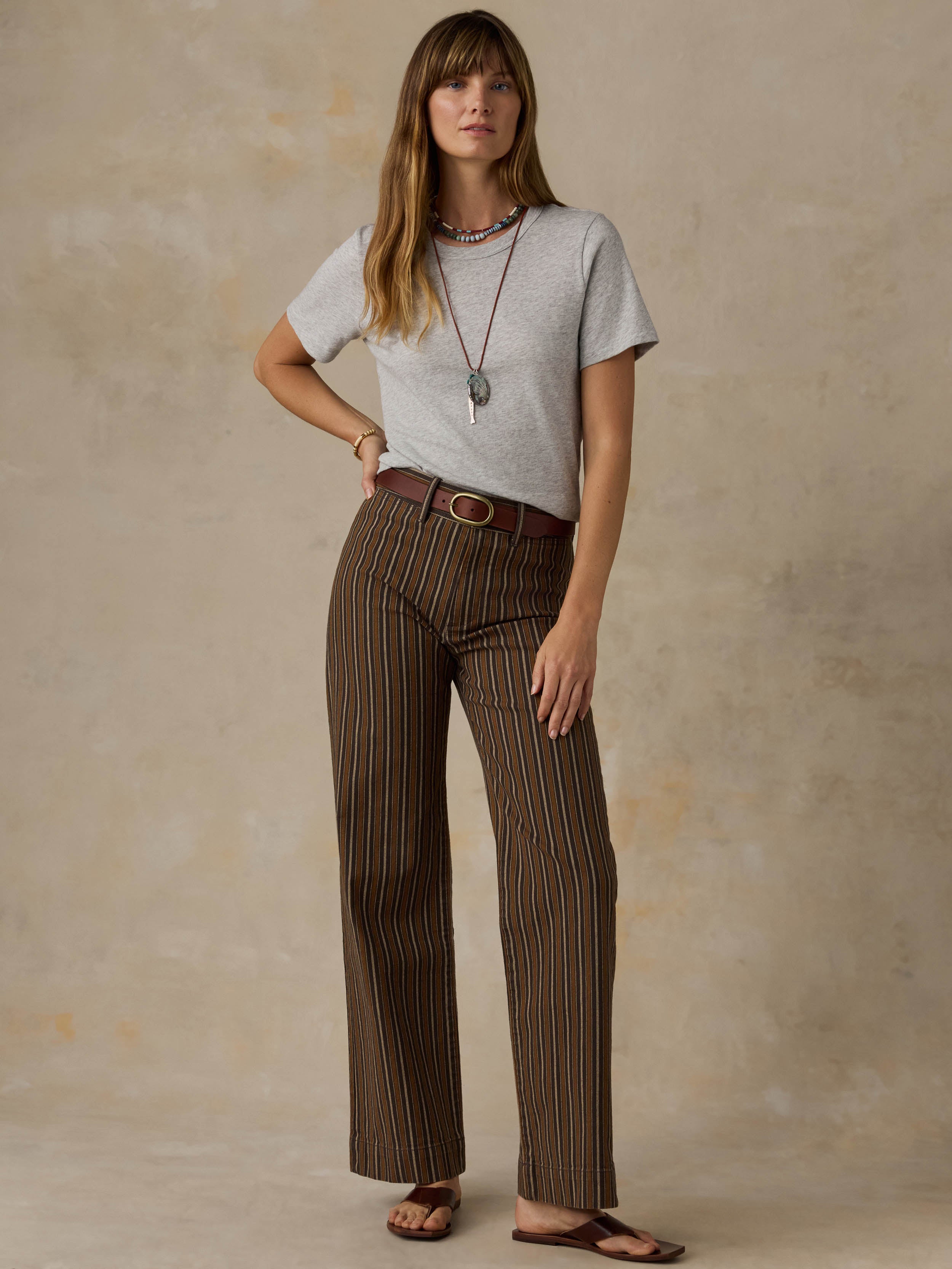 A woman wearing a grey t-shirt and striped pants against a beige background