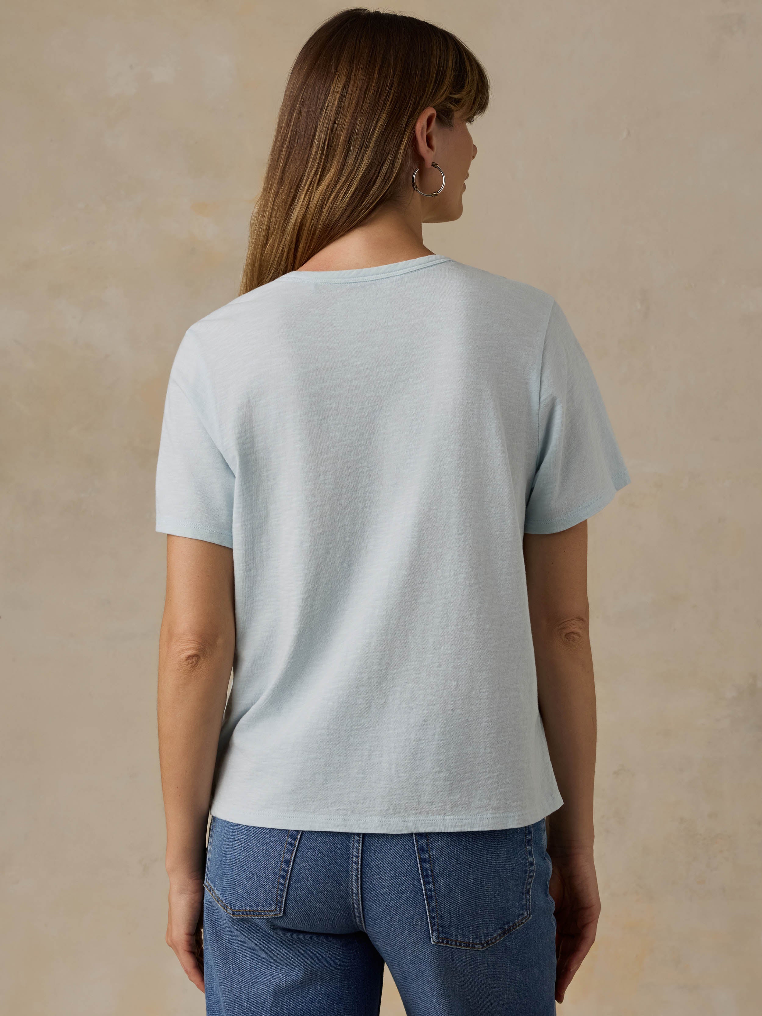 Woman wearing a light blue t-shirt and blue jeans against a beige background