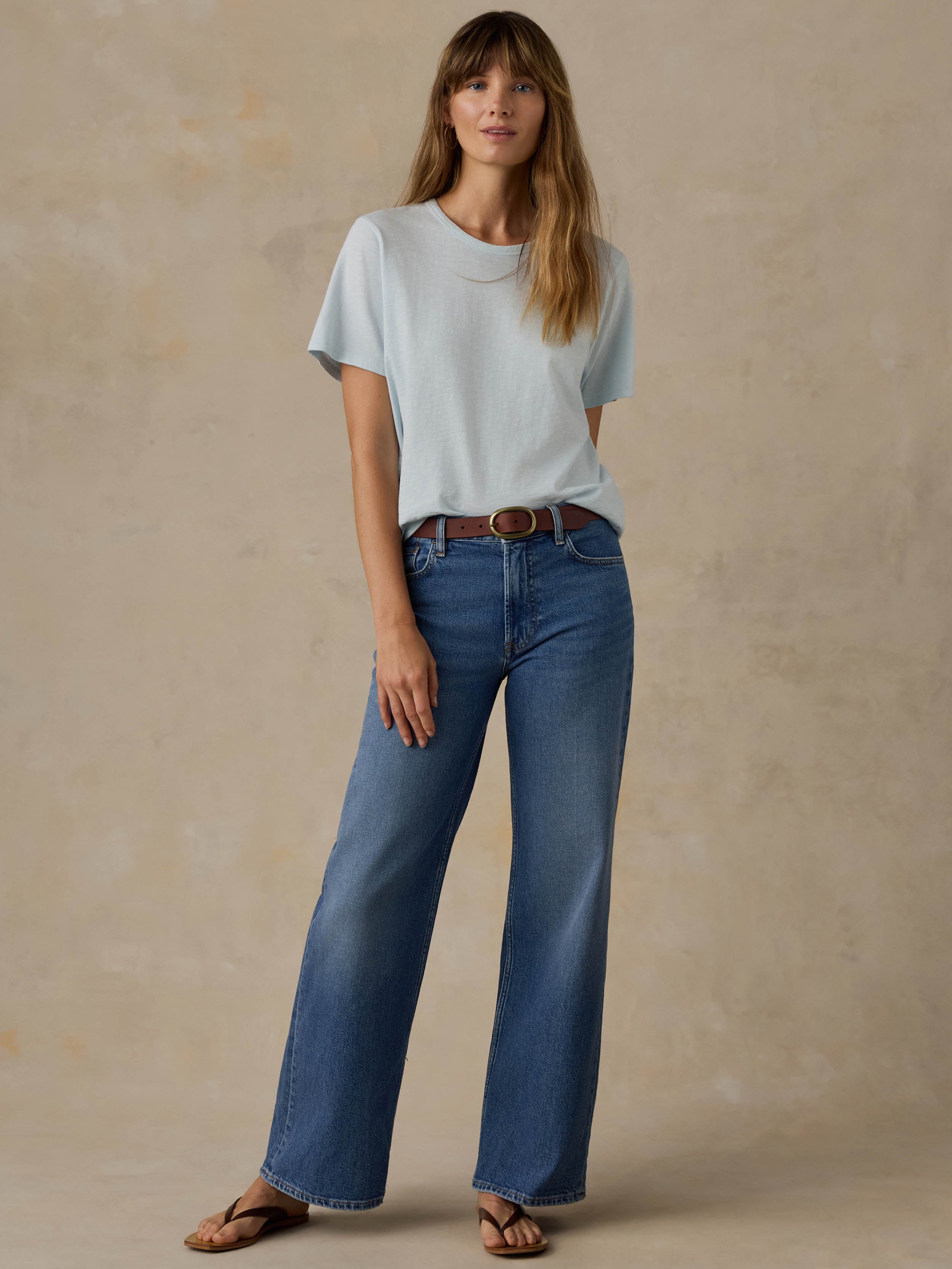 Woman wearing a light blue t-shirt and blue jeans against a beige background