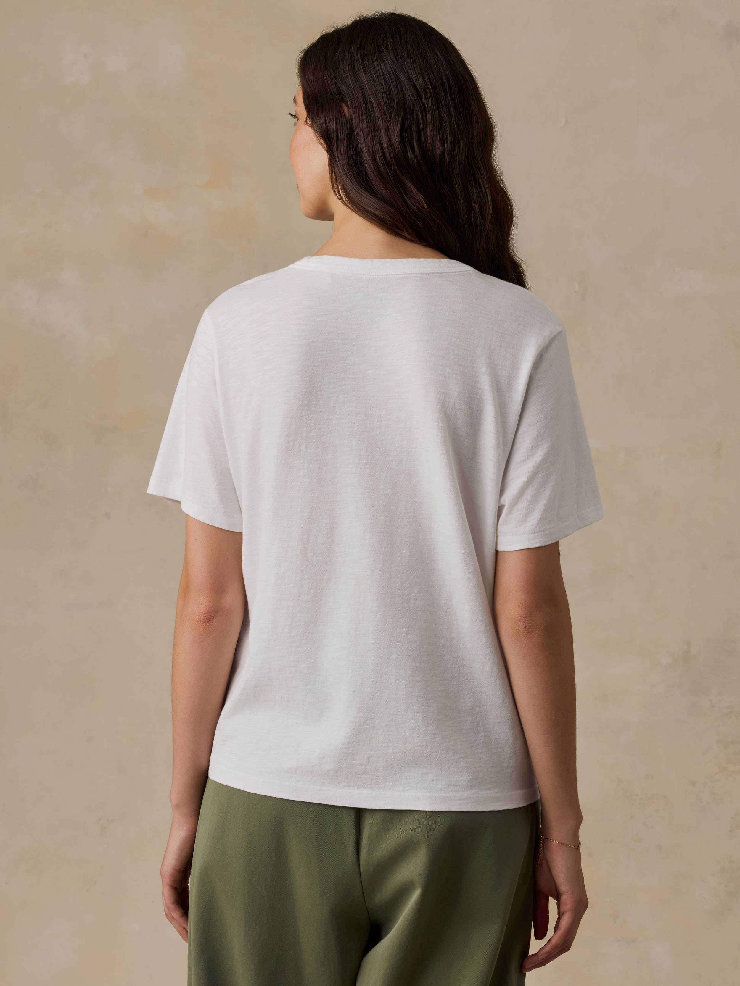 Woman wearing a white t-shirt and green pants against a beige background