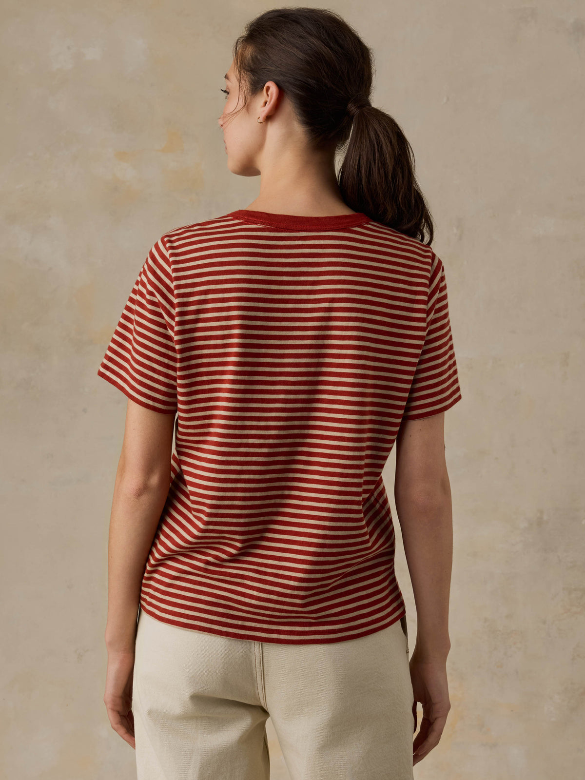 Woman wearing a red striped shirt and beige pants against a beige background, image 5 of 8