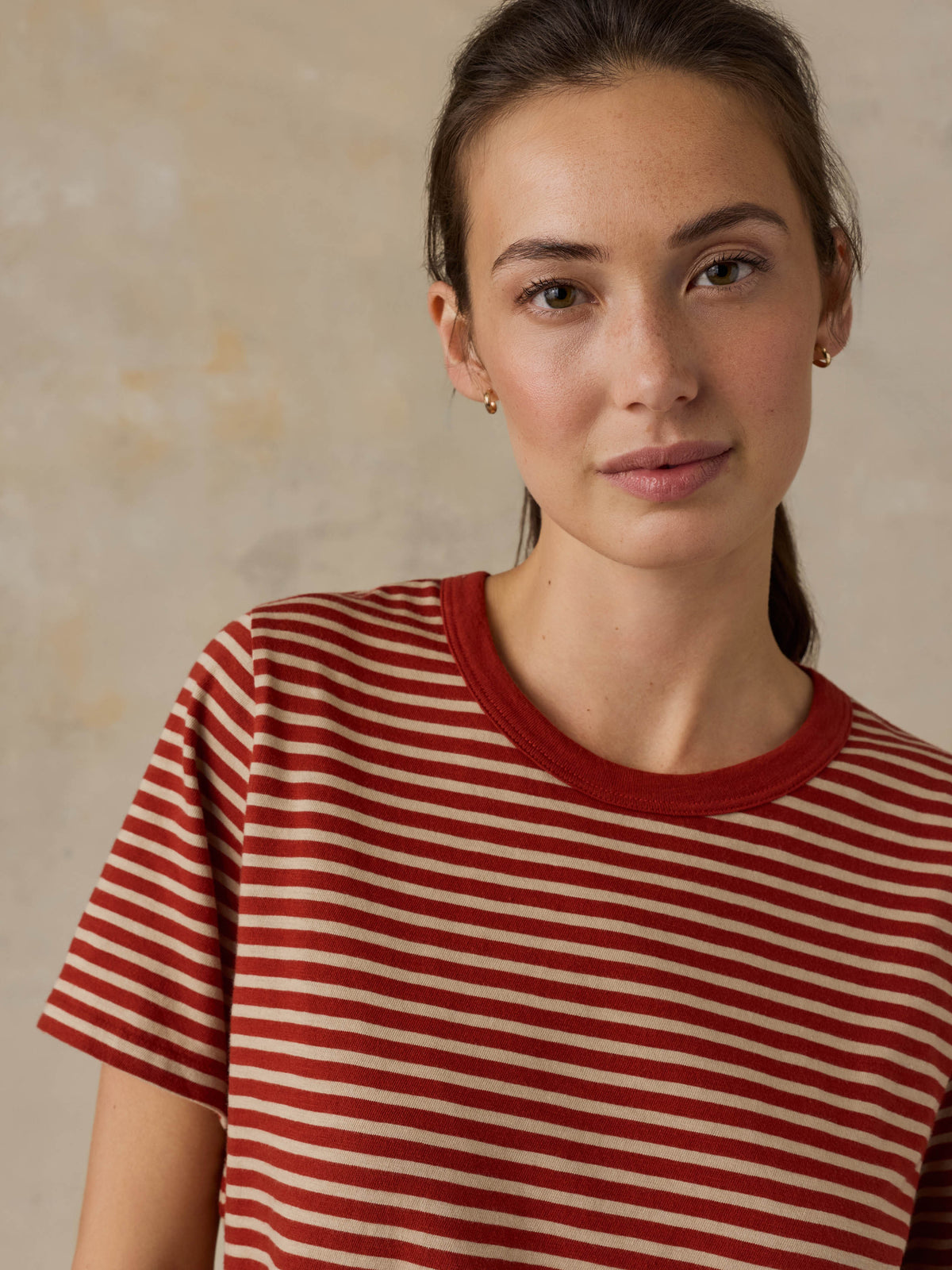 Woman wearing a red striped shirt against a beige background, image 2 of 8