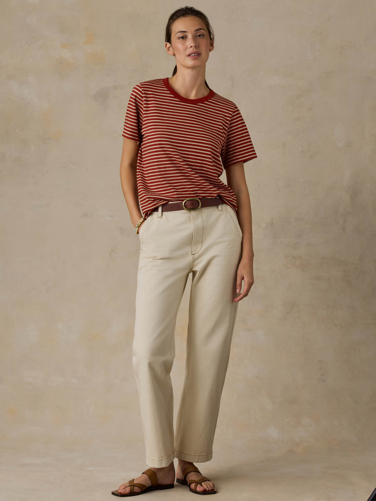 Woman wearing a red striped shirt and beige pants against a beige background, image 8 of 8