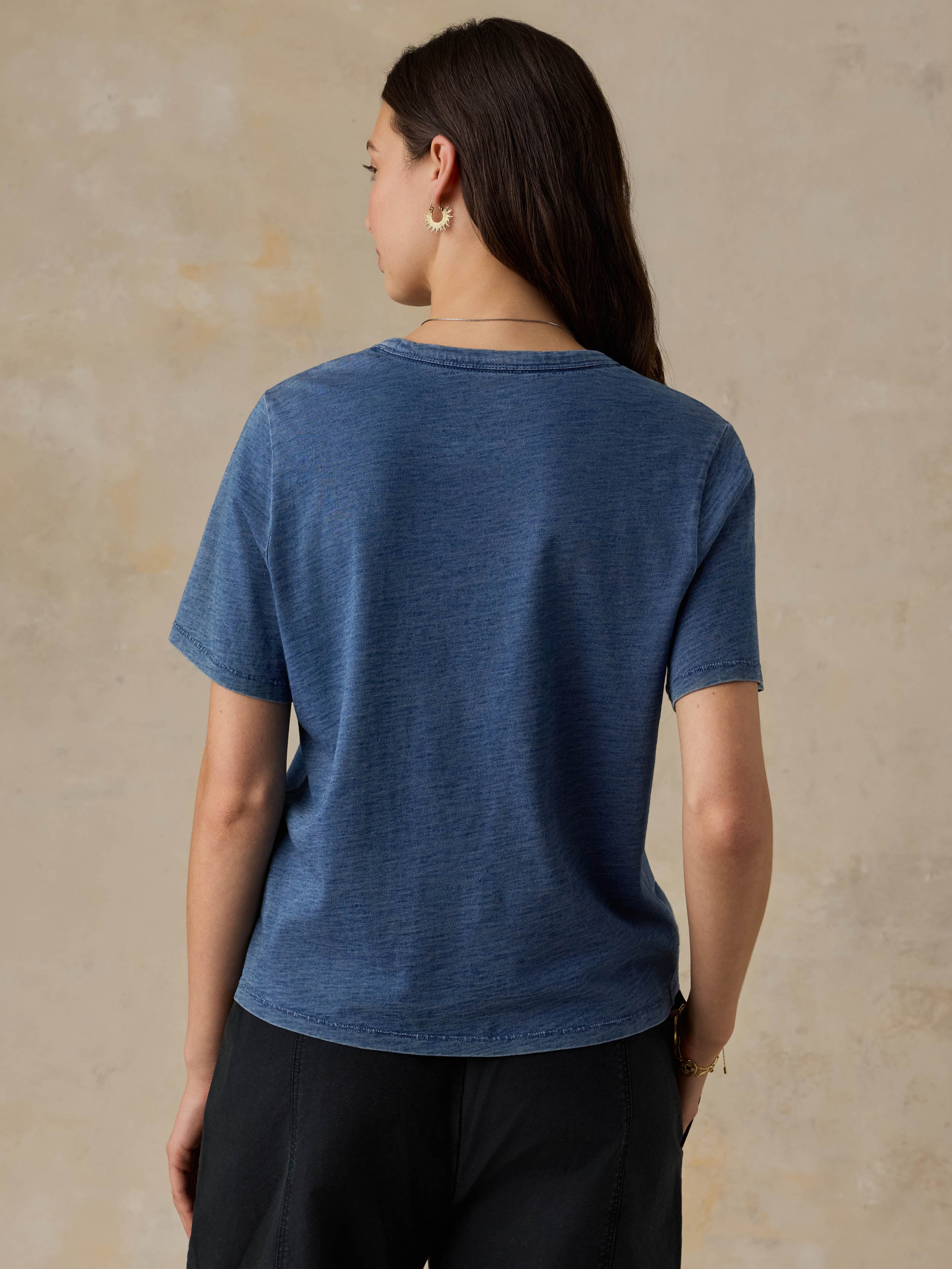 Woman wearing a blue t-shirt and black pants against a beige background
