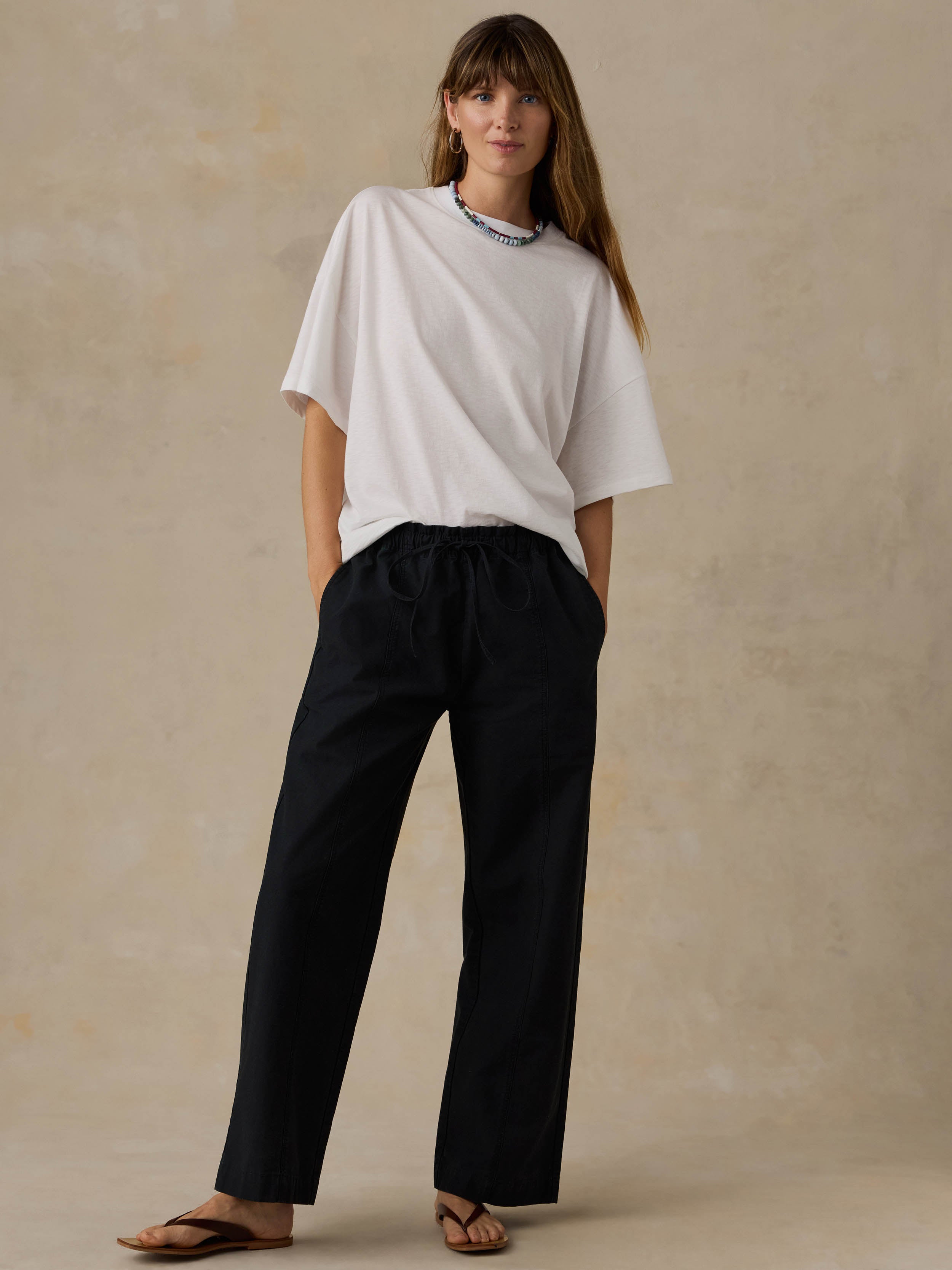 Woman wearing a white t-shirt and black pants against a beige background