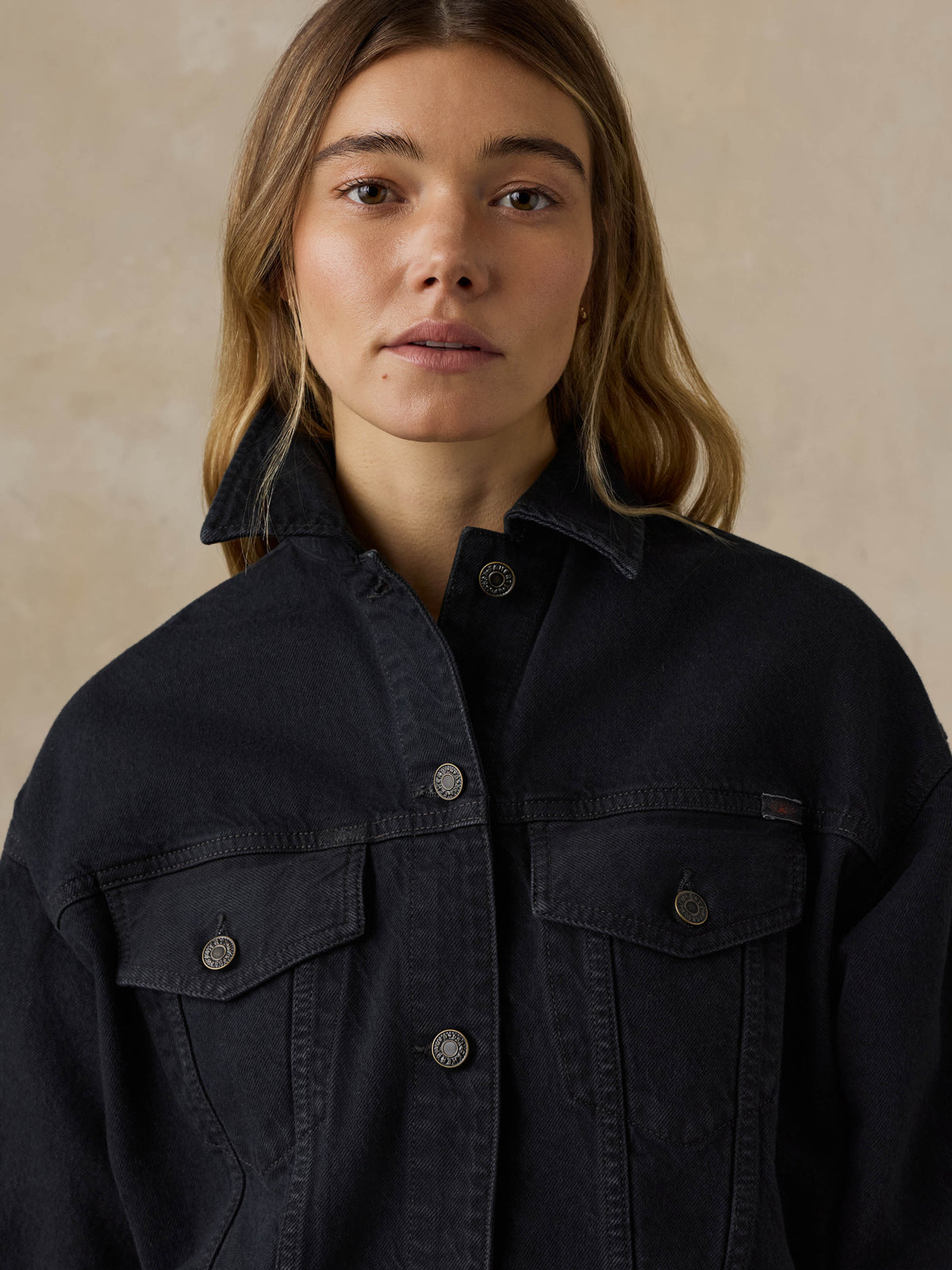 Woman wearing a black denim jacket against a beige background, image 4 of 5