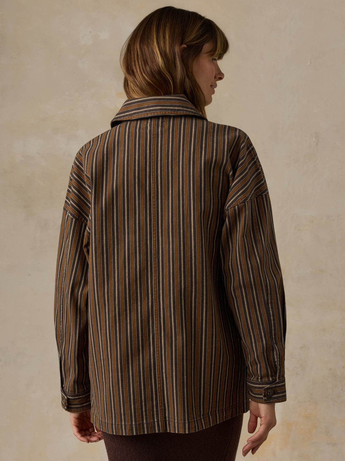 Woman wearing a brown striped chore jacket against a beige background, image 4 of 6