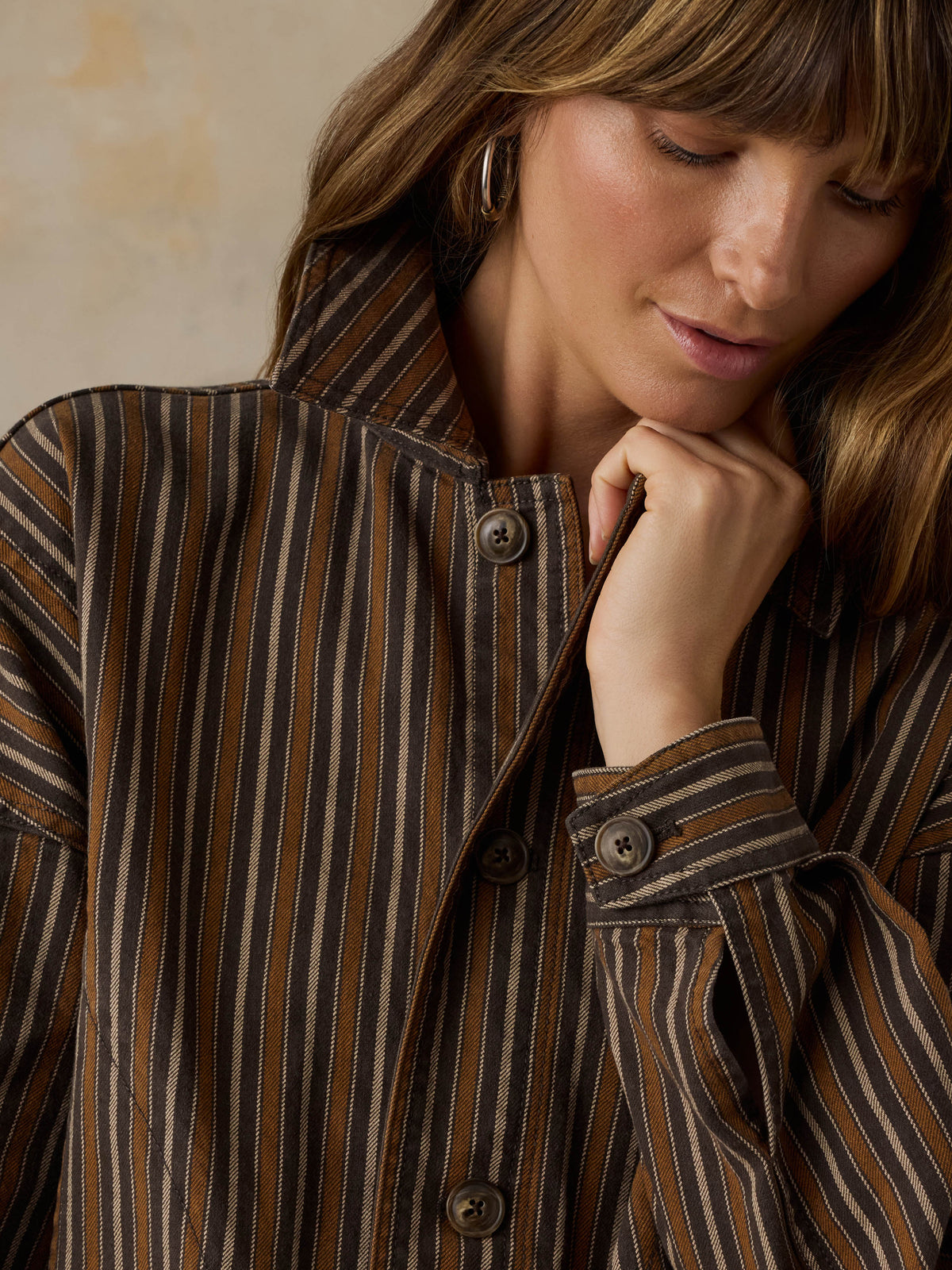 Woman wearing a brown striped chore jacket against a beige background, image 5 of 6