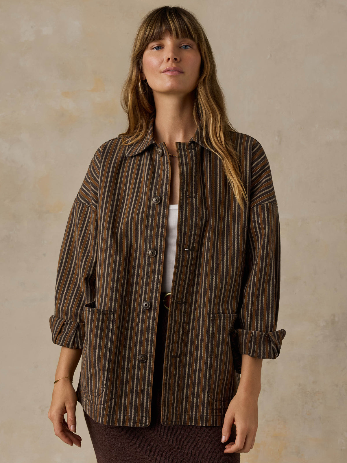 Woman wearing a brown striped chore jacket against a beige background, image 1 of 6