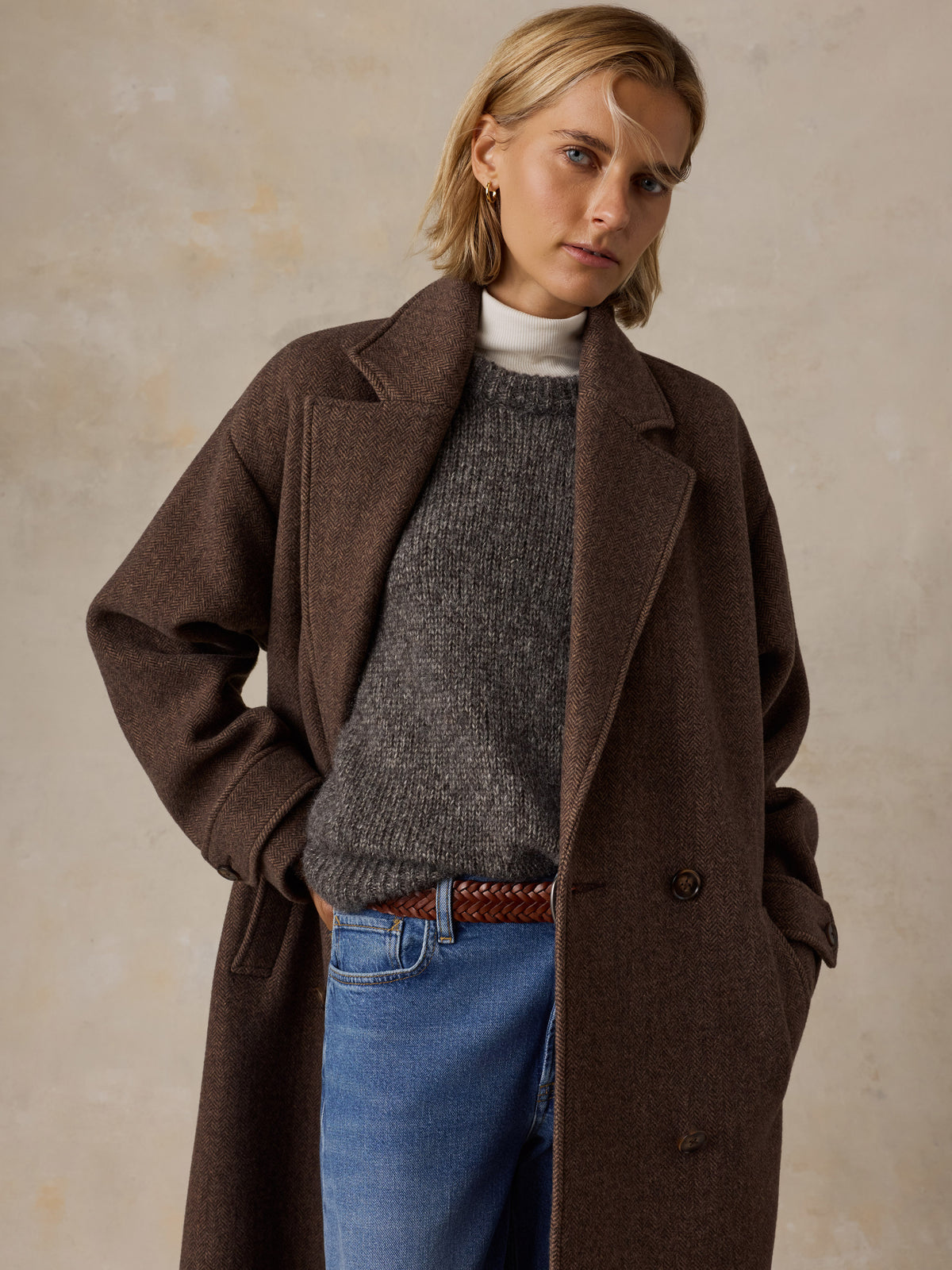 A woman wearing a brown long coat over a sweater and blue jeans, image 6 of 9
