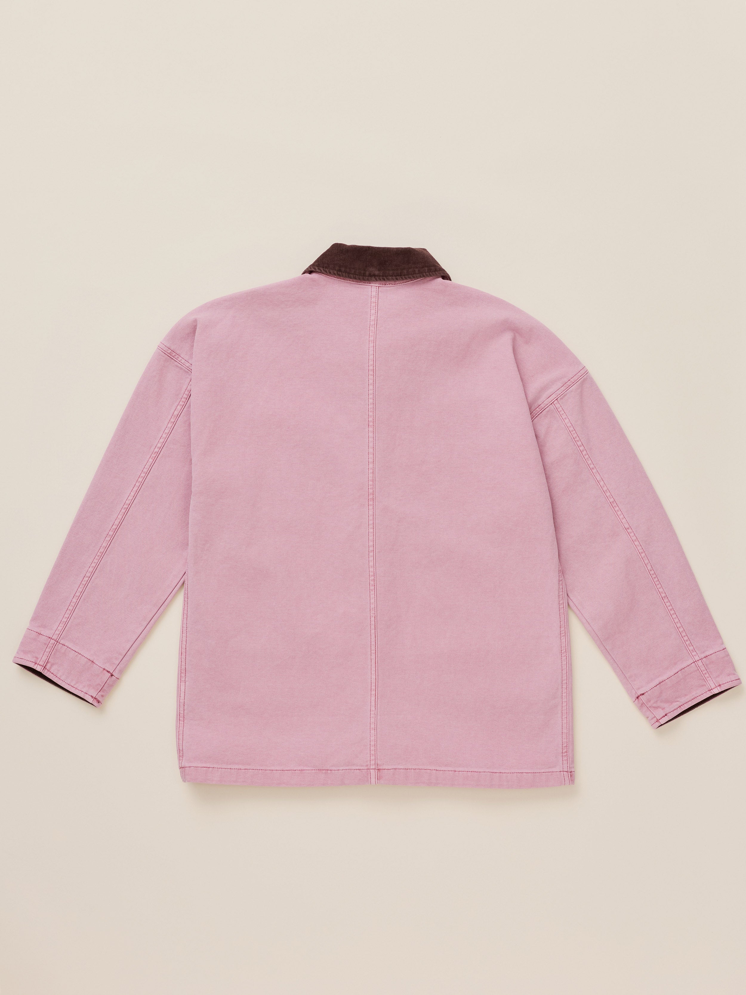 A light pink canvas jacket shown from the back, featuring a contrasting dark brown corduroy collar, laid flat on a warm beige background.