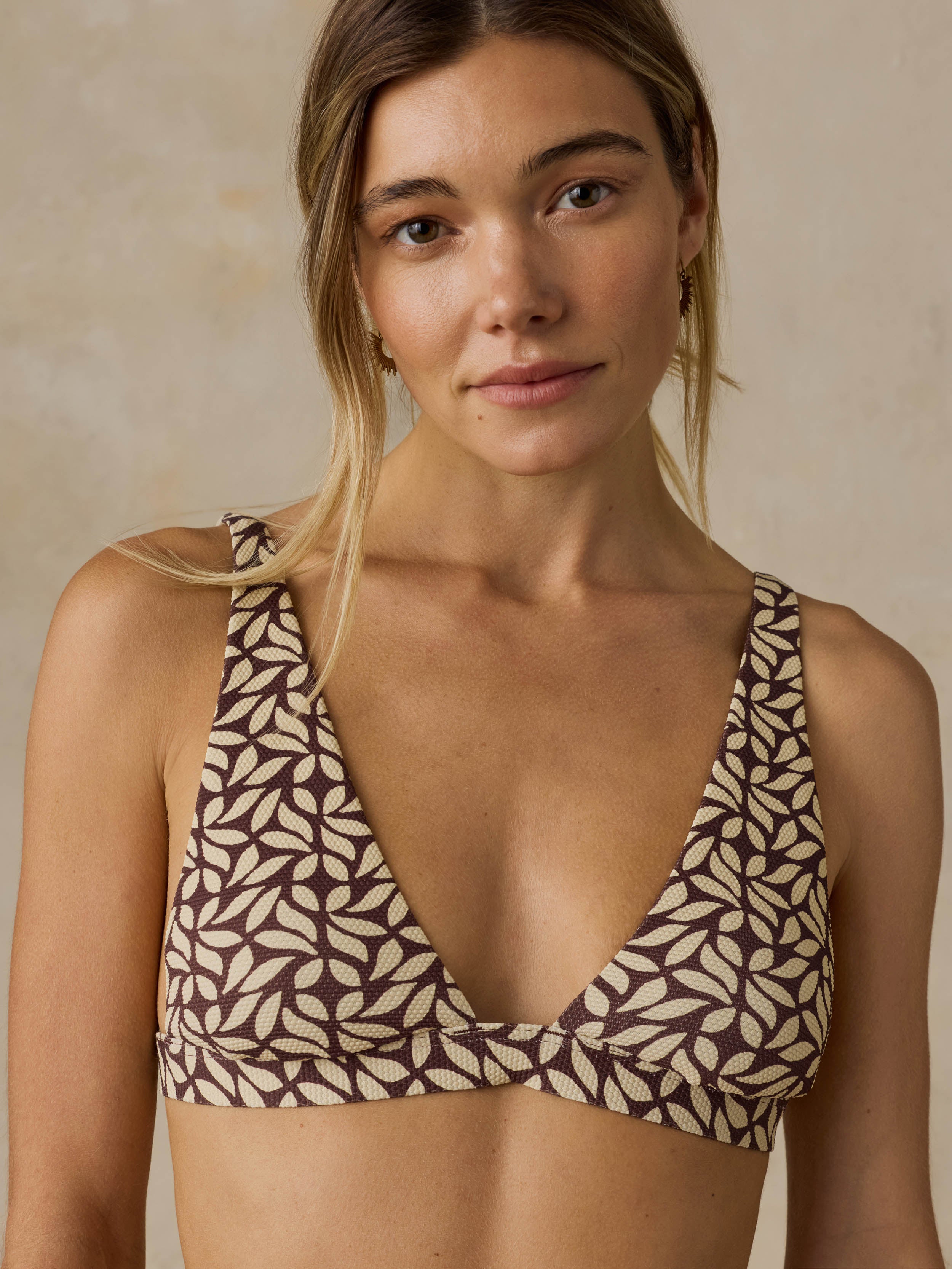 Woman wearing a brown printed swim suit  topagainst a beige background