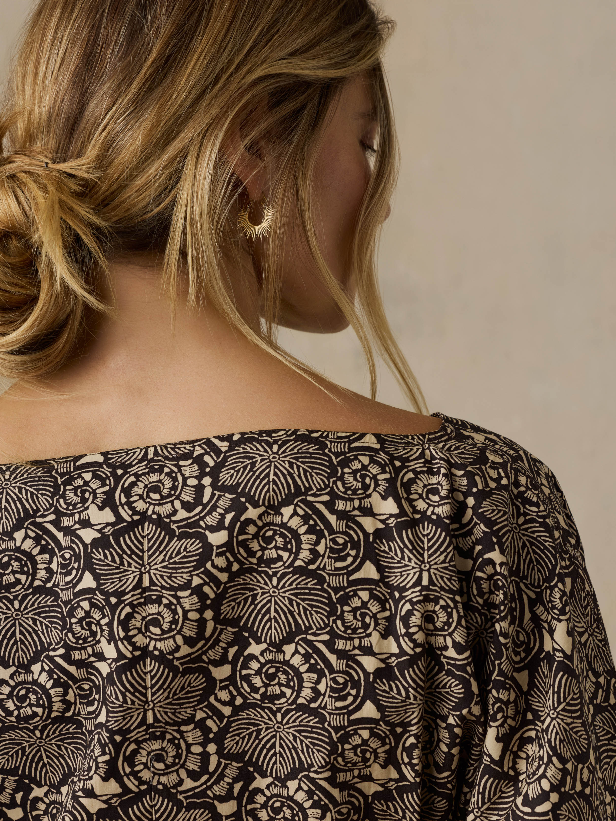 Woman wearing a black patterned blouse against a beige background