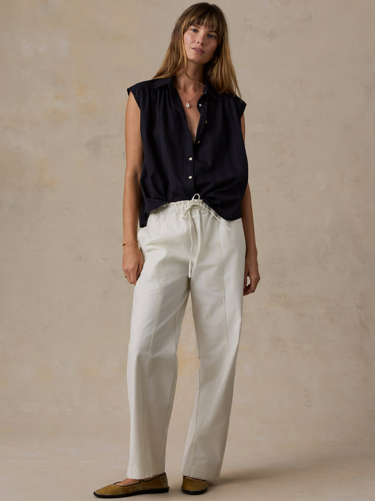 Woman wearing a black shirt and white pants against a beige background, image 5 of 5