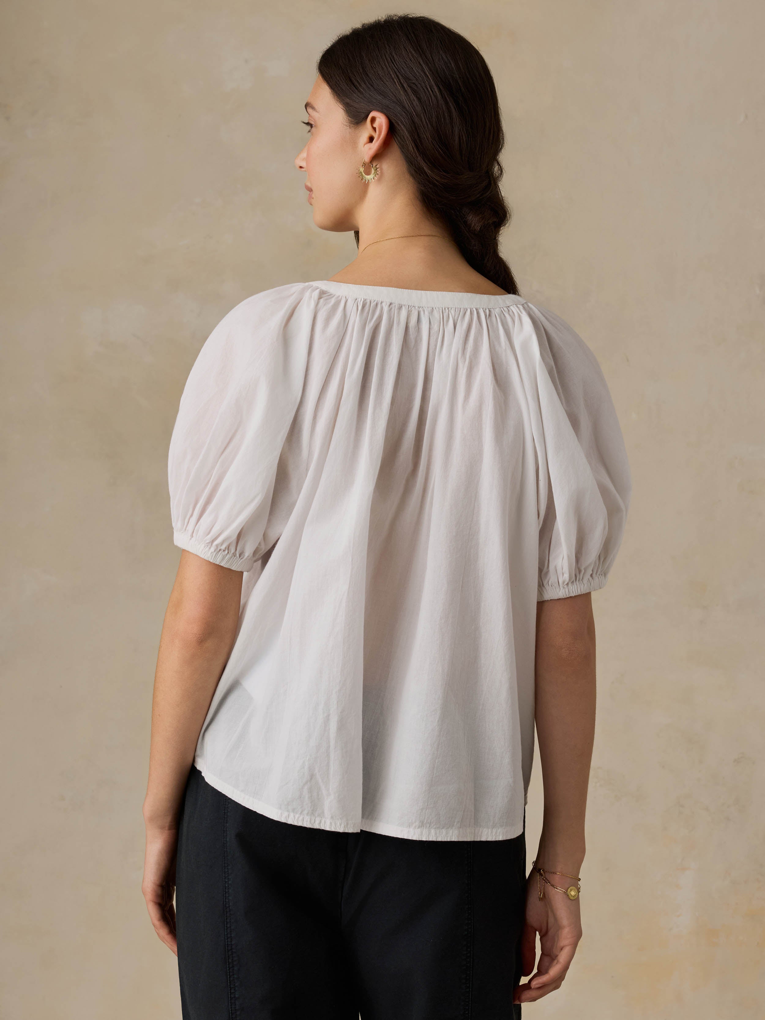 Woman wearing a white blouse with puff sleeves against a beige background