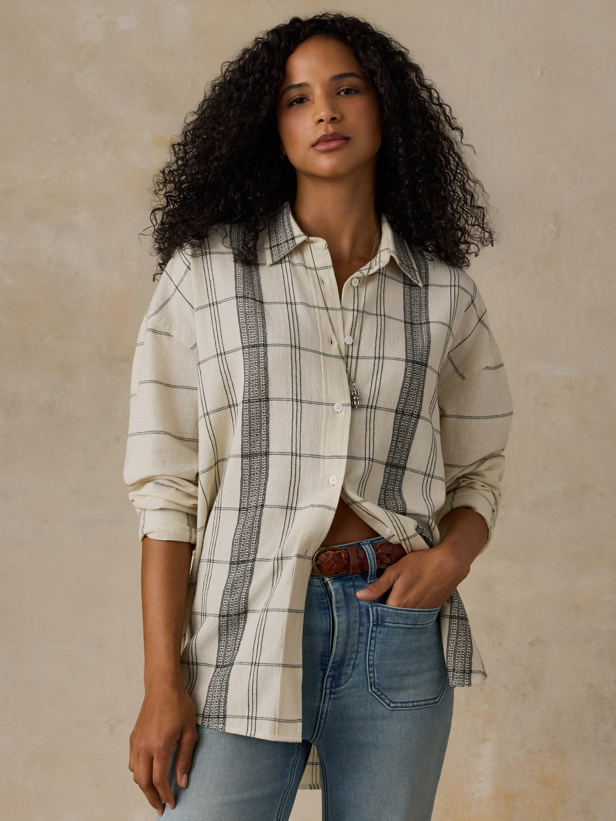 Woman wearing a white and black plaid shirt with blue jeans against a beige background, image 1 of 6