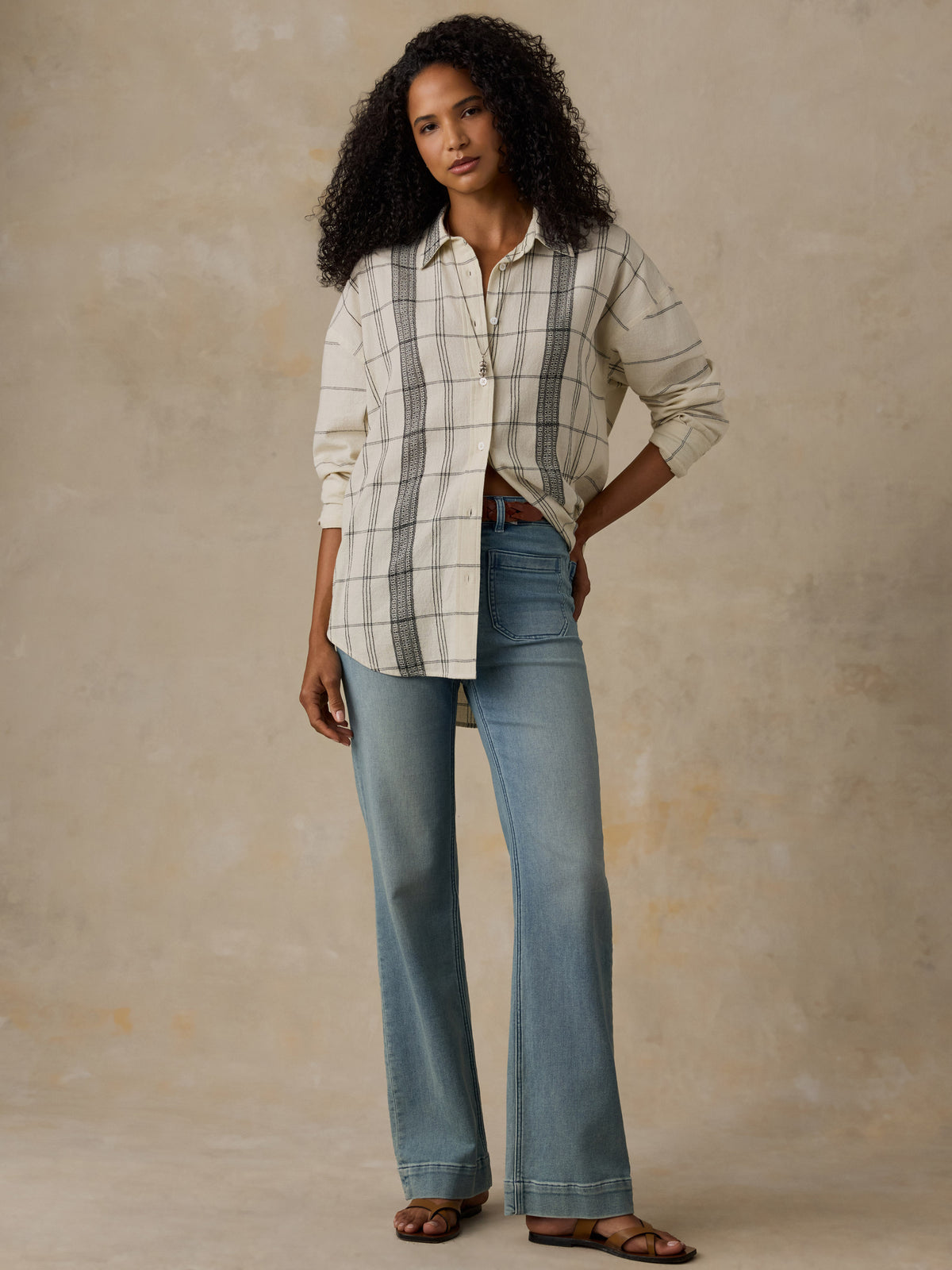 Woman wearing a white and black plaid shirt with blue jeans against a beige background, image 6 of 6
