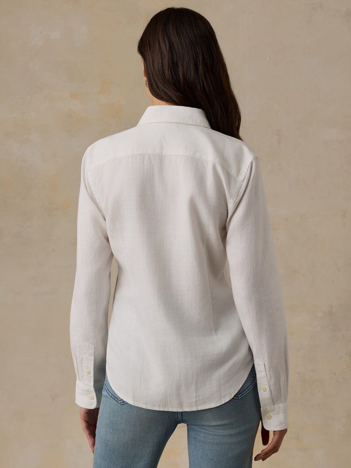 Woman wearing a white chambray button down shirt and blue jeans against a beige background, image 3 of 5
