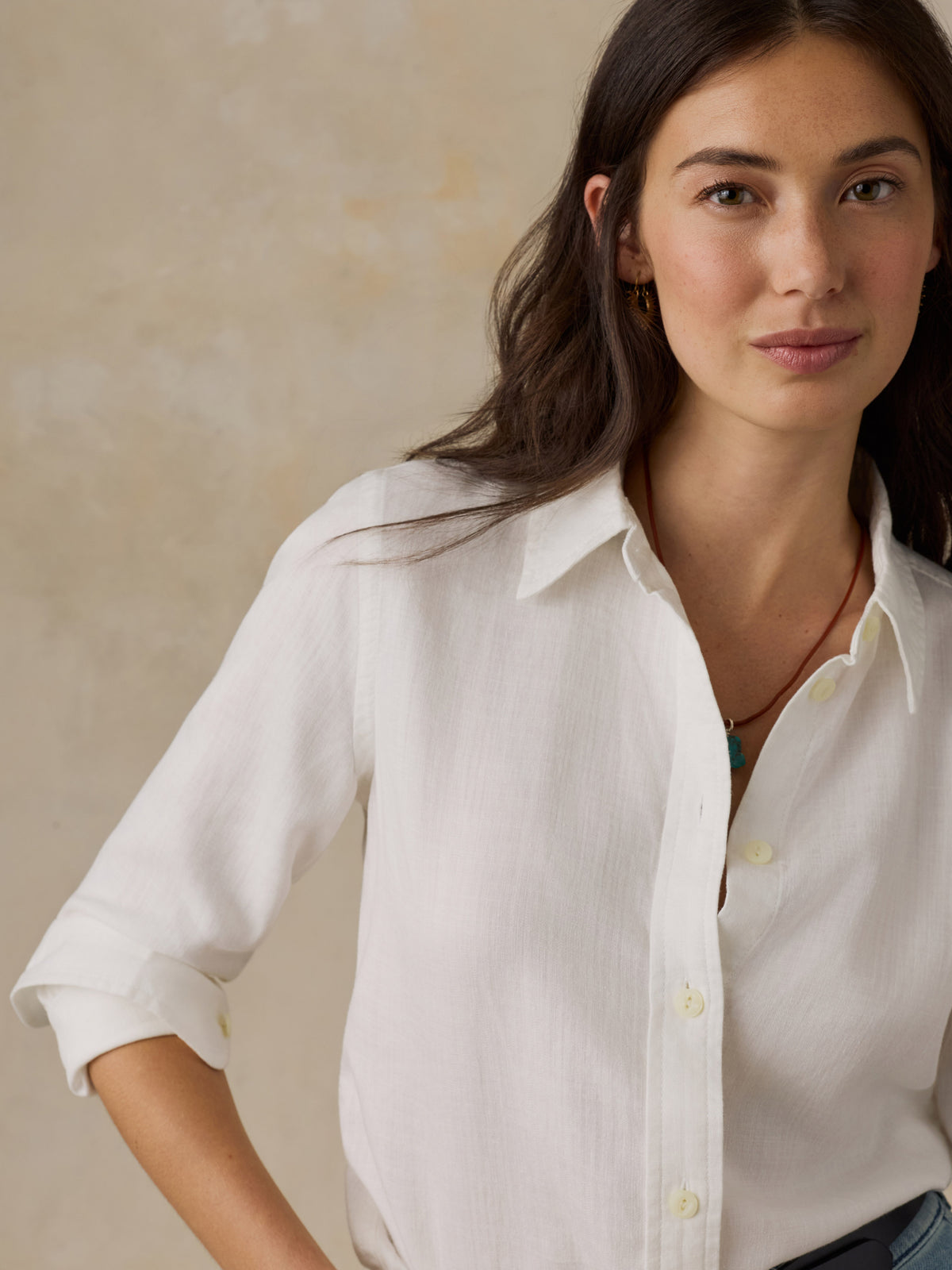 Woman wearing a white chambray button down shirt against a beige background, image 5 of 5