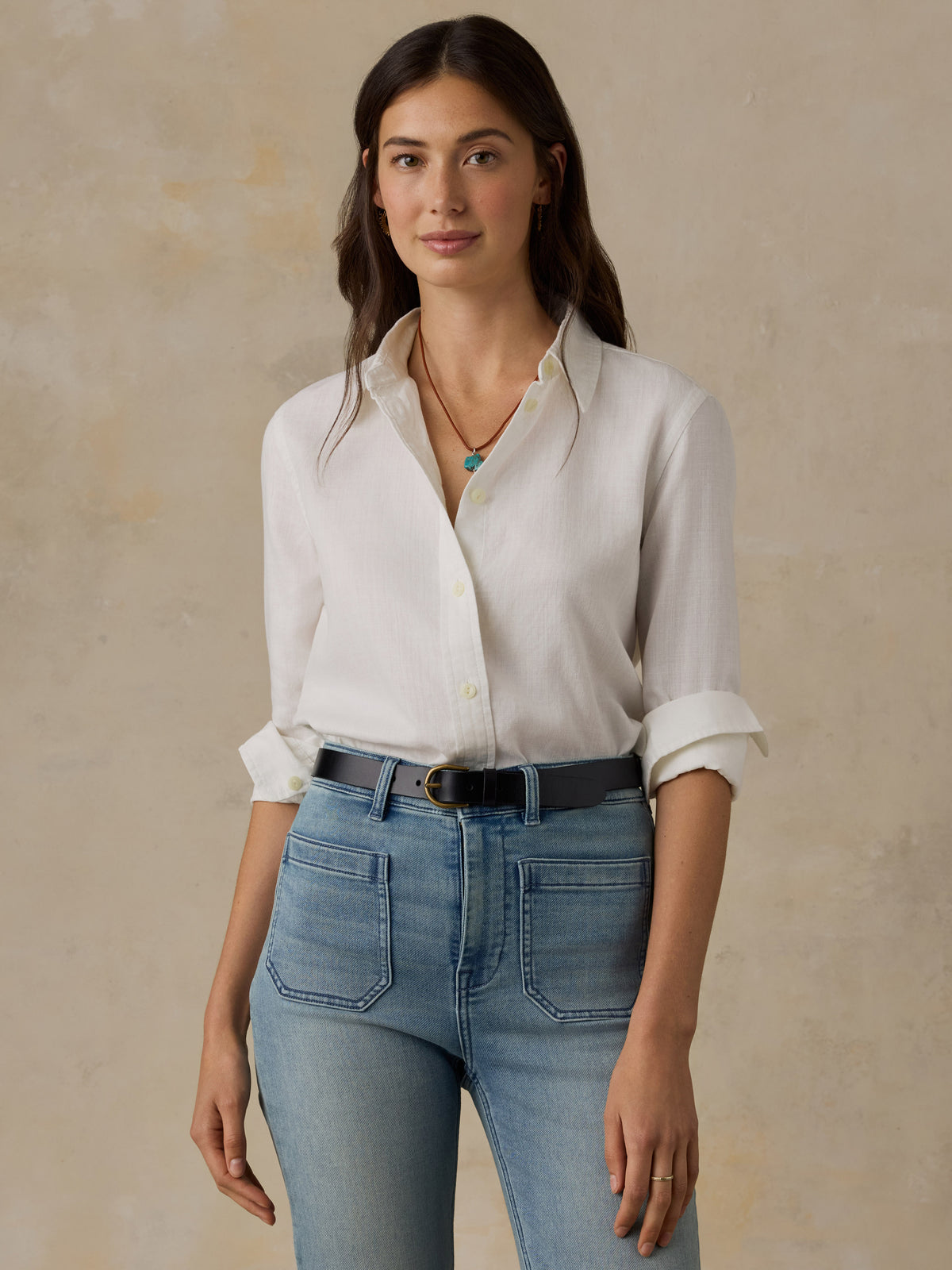 Woman wearing a white chambray button down shirt and blue jeans against a beige background, image 1 of 5