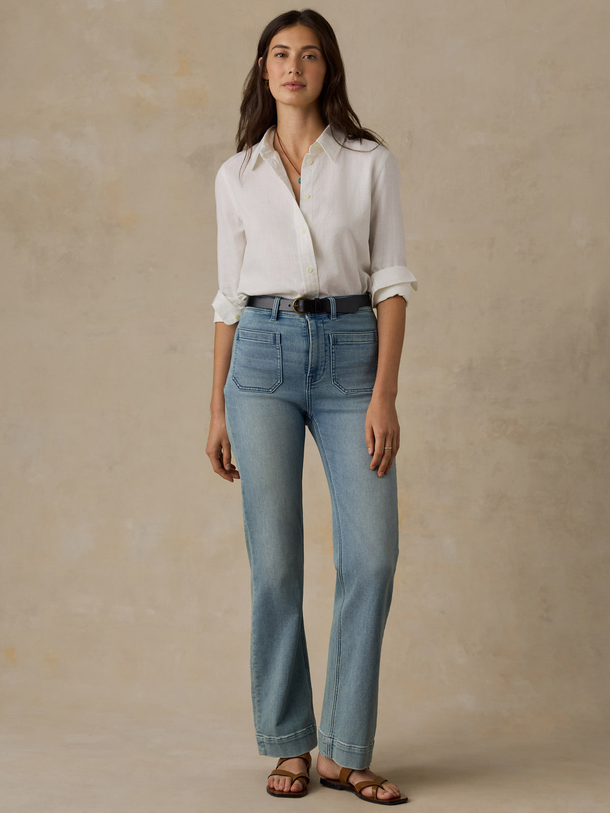 Woman wearing a white chambray button down shirt and blue jeans against a beige background, image 4 of 5