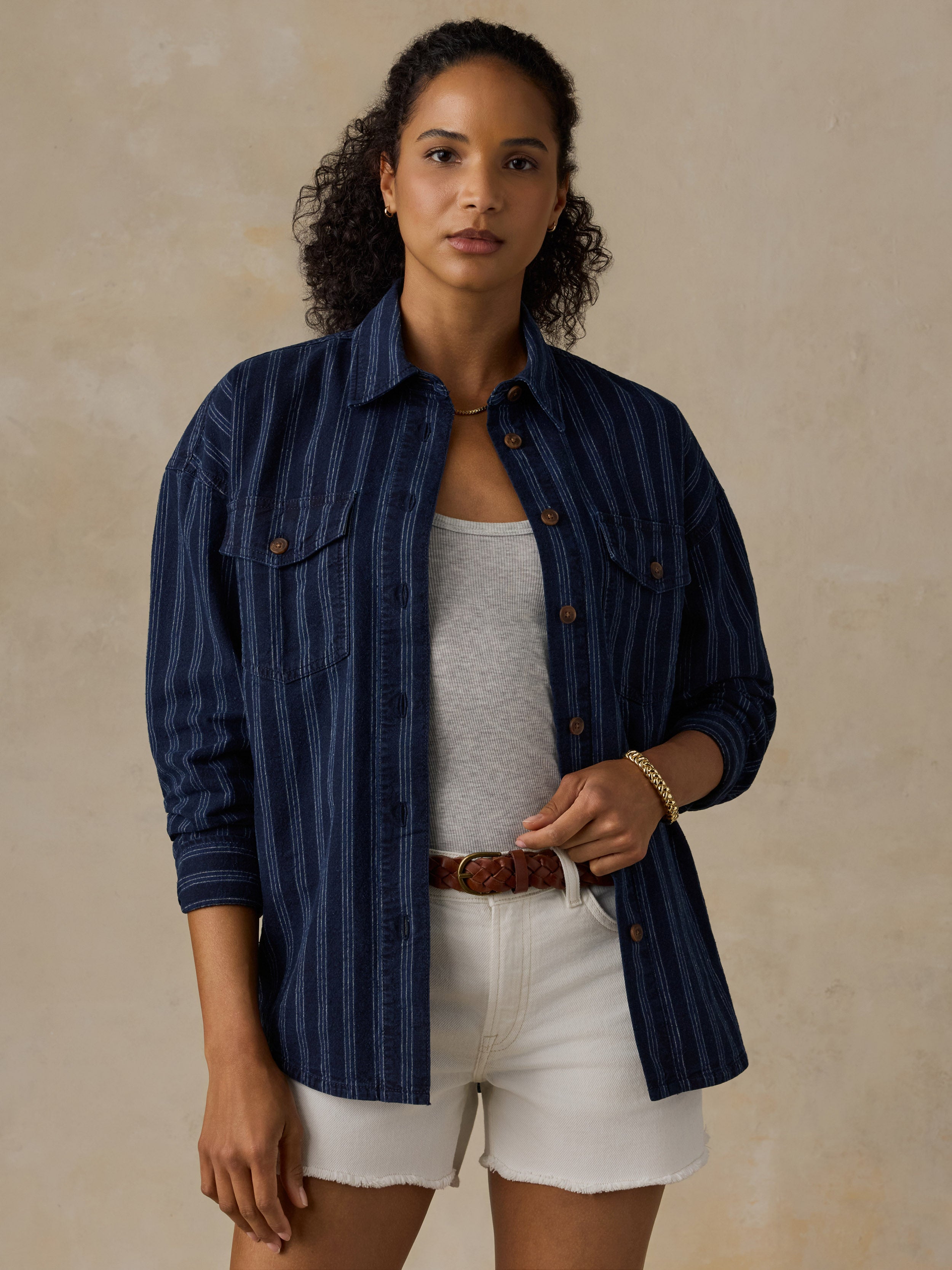 Woman wearing a navy striped overshirt with white denim shorts against a beige background