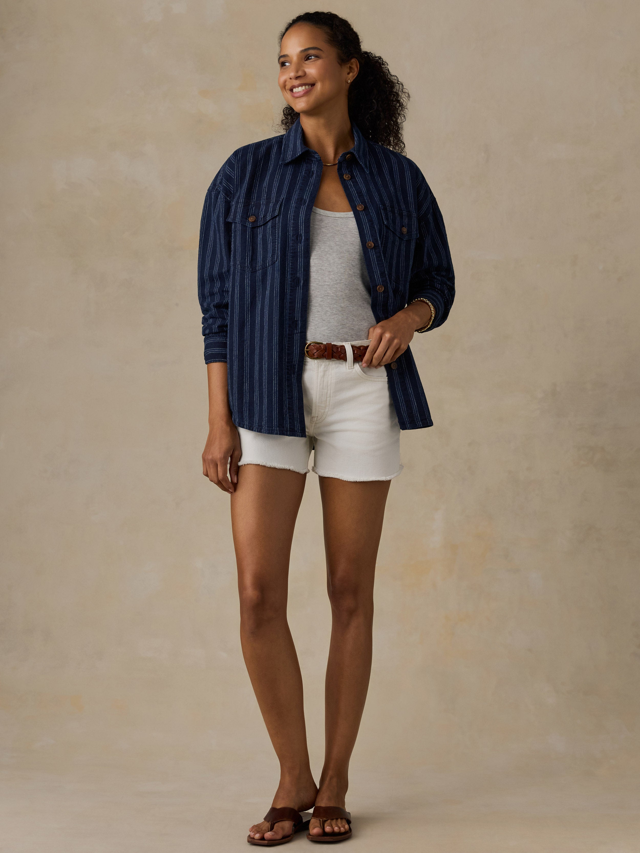 Woman wearing a navy striped overshirt with white denim shorts against a beige background