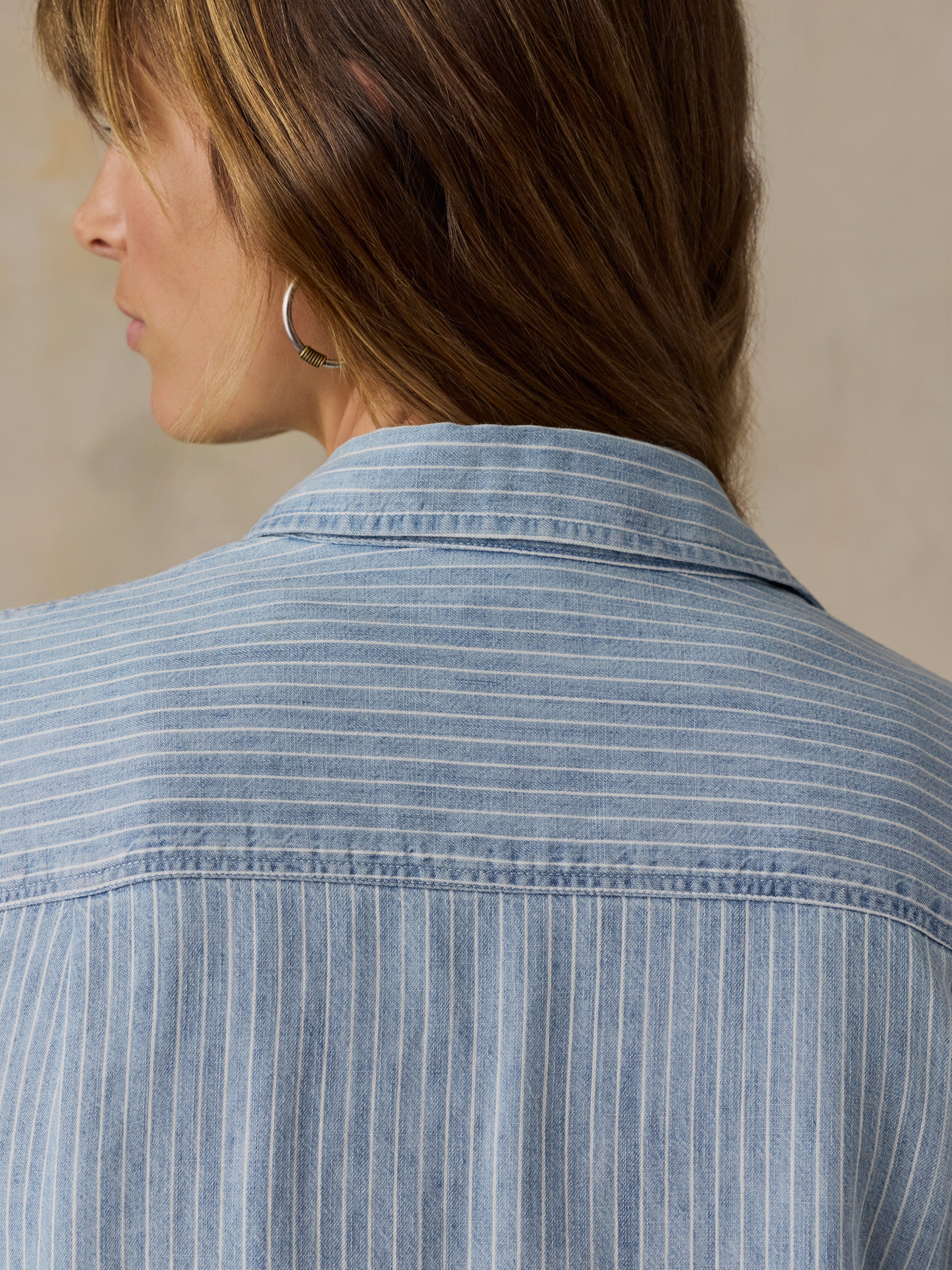 Woman wearing a blue and white striped chambray button down shirt against a beige background