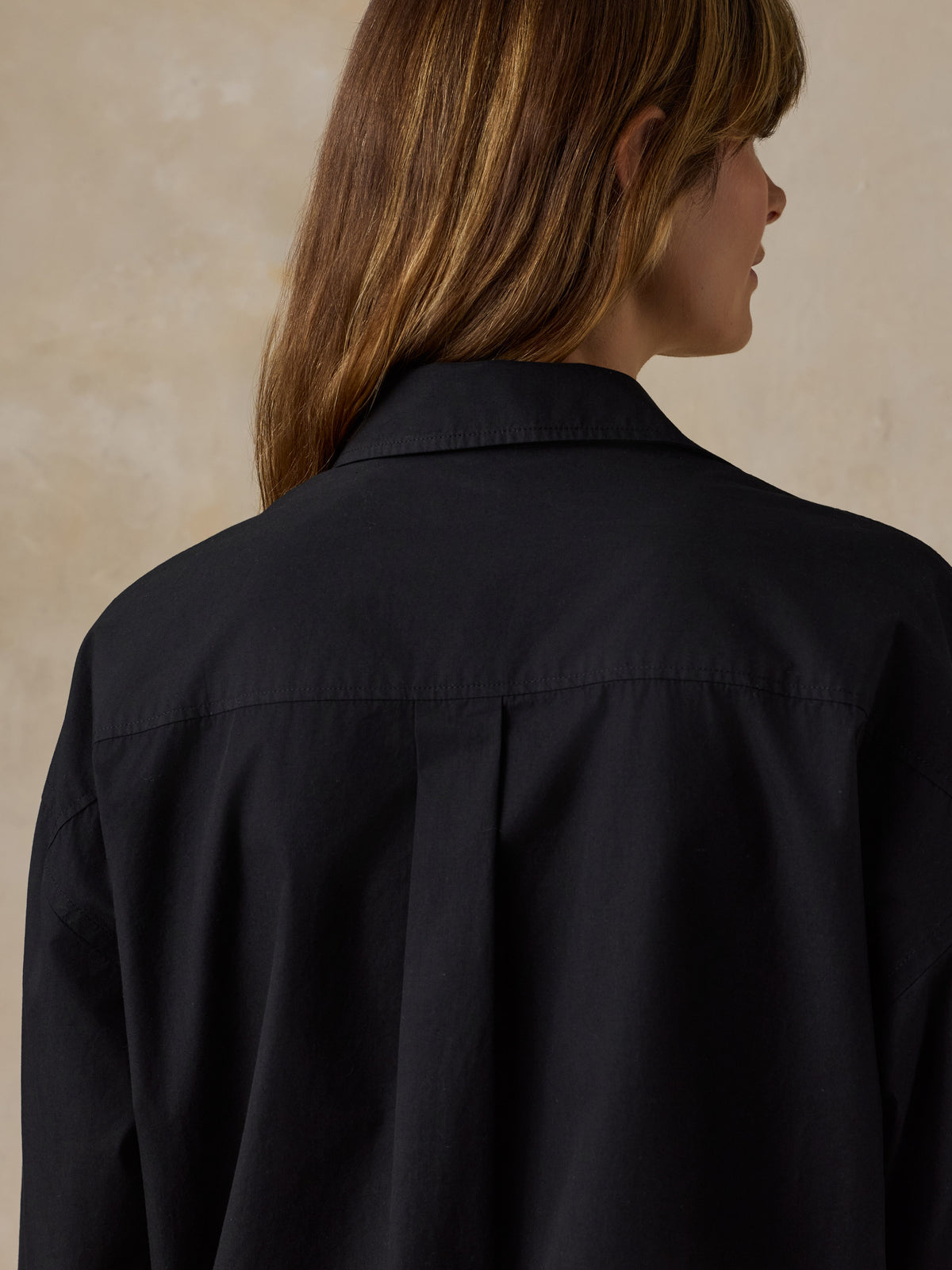 Woman wearing a black button down shirt against a beige background, image 6 of 6