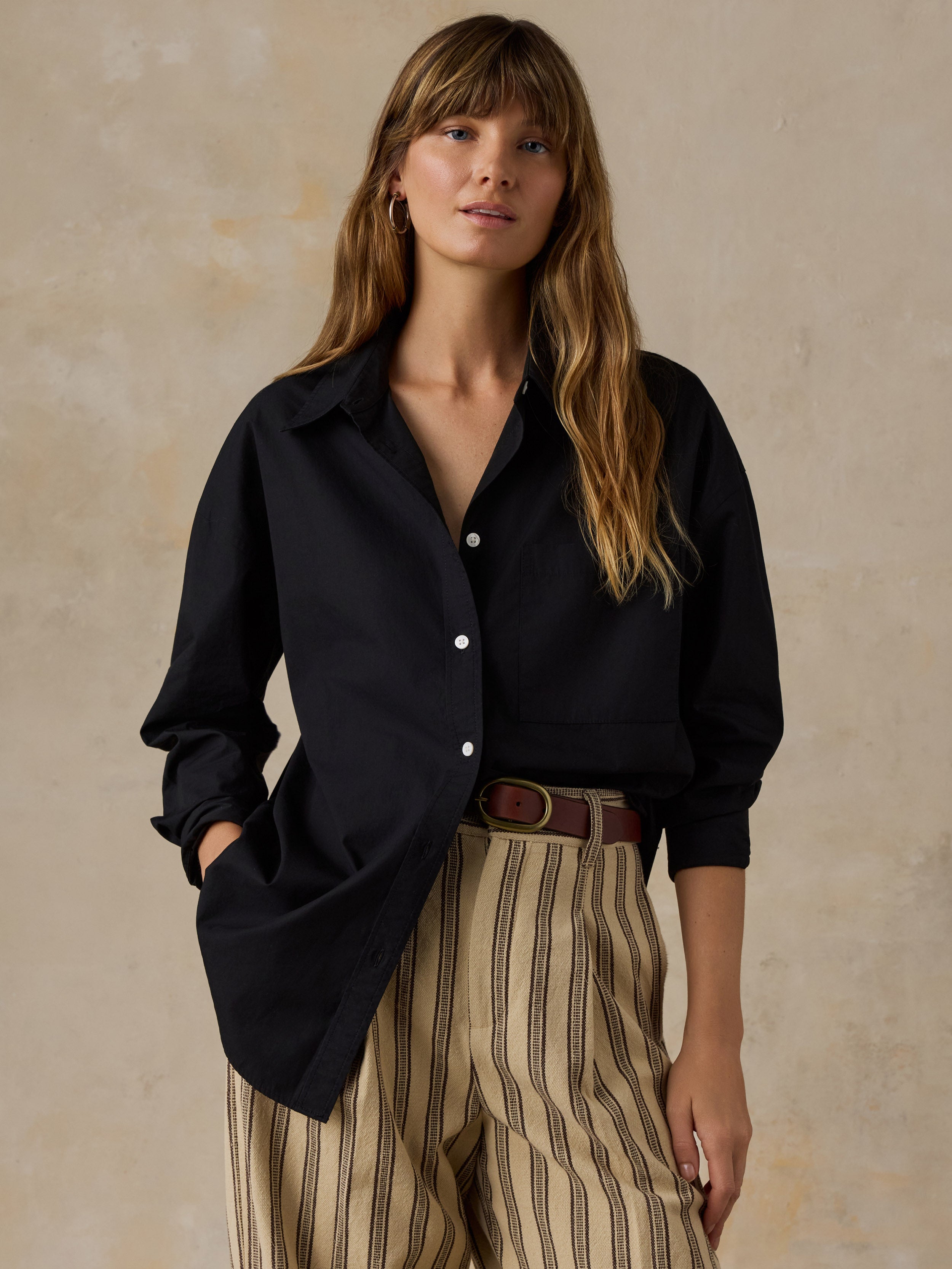 Woman wearing a black button down shirt and beige striped pants against a beige background