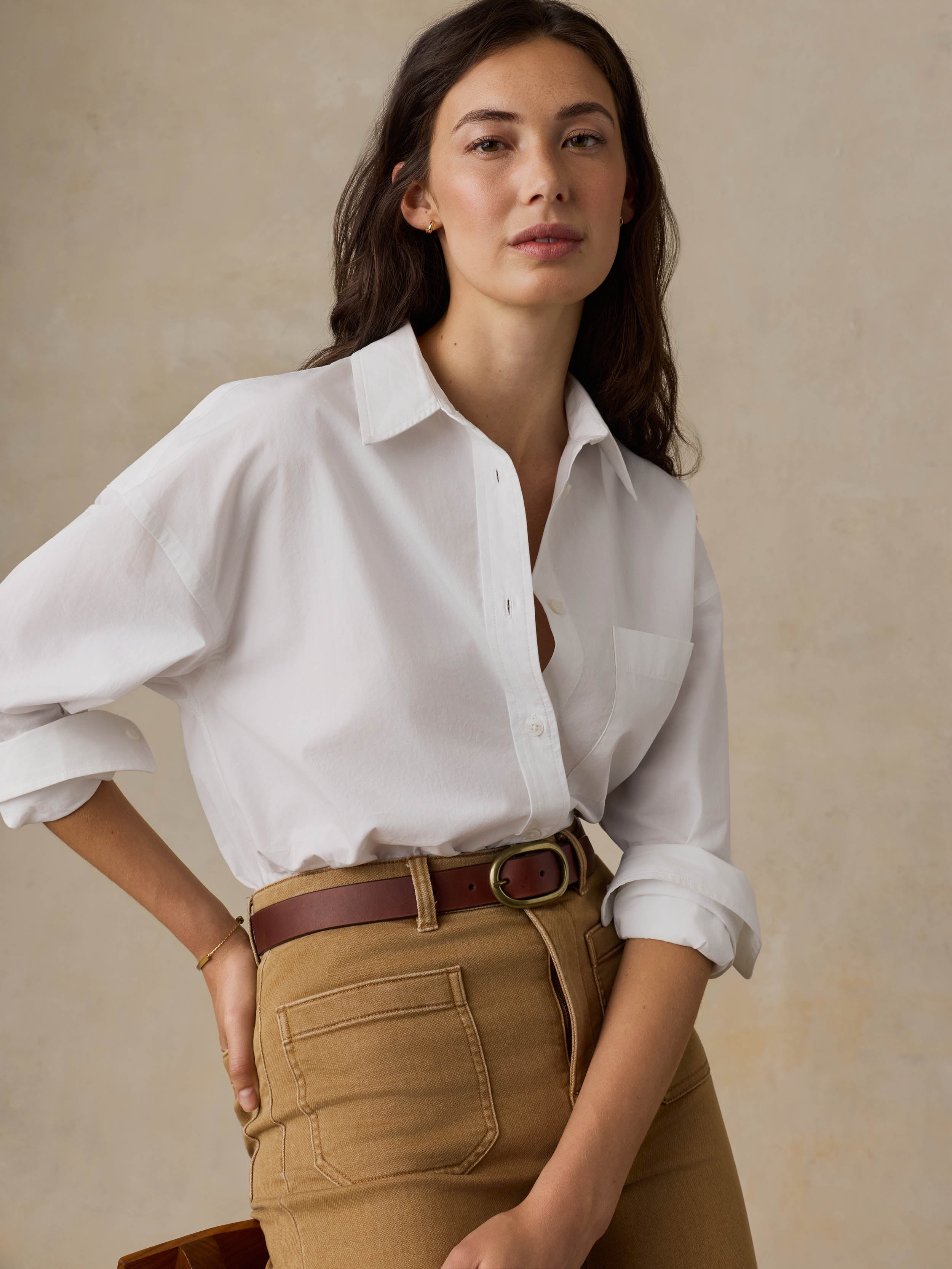 Woman wearing a white shirt and brown pants against a beige background