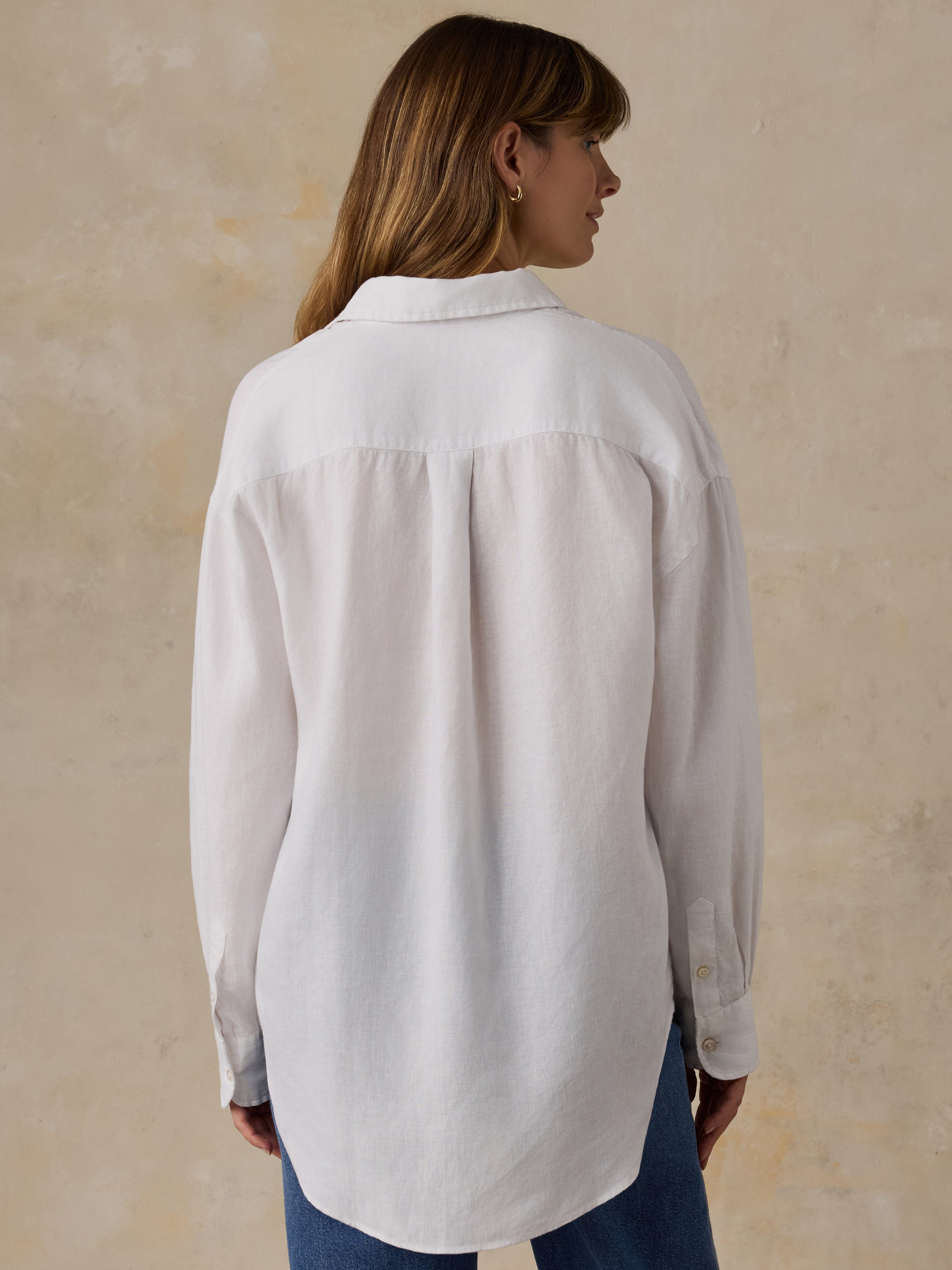 Woman wearing a white linen button down shirt with blue jeans against a beige background