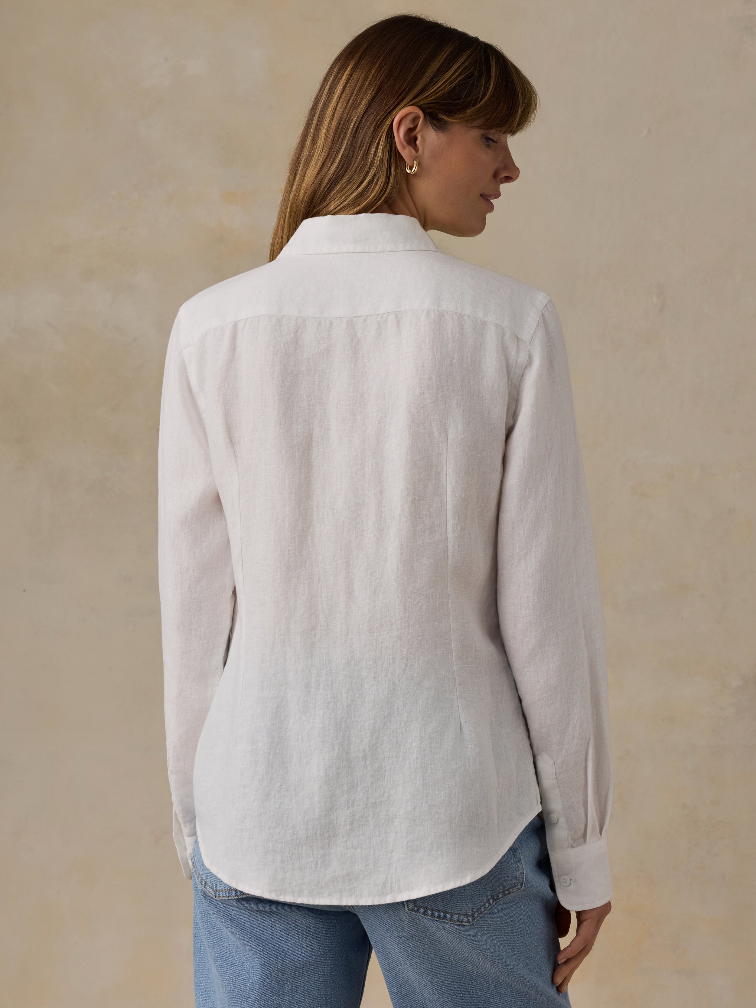 Woman wearing a white linen shirt and blue jeans against a beige background