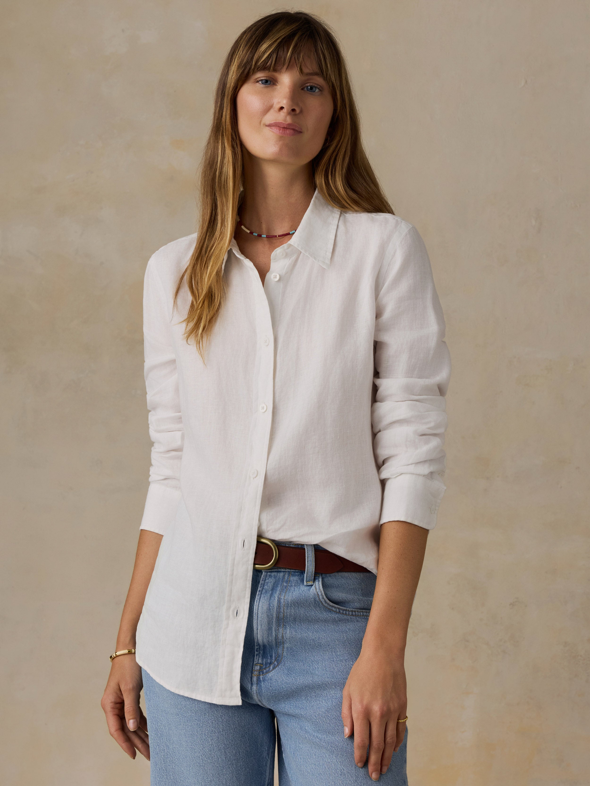 Woman wearing a white linen shirt and blue jeans against a beige background