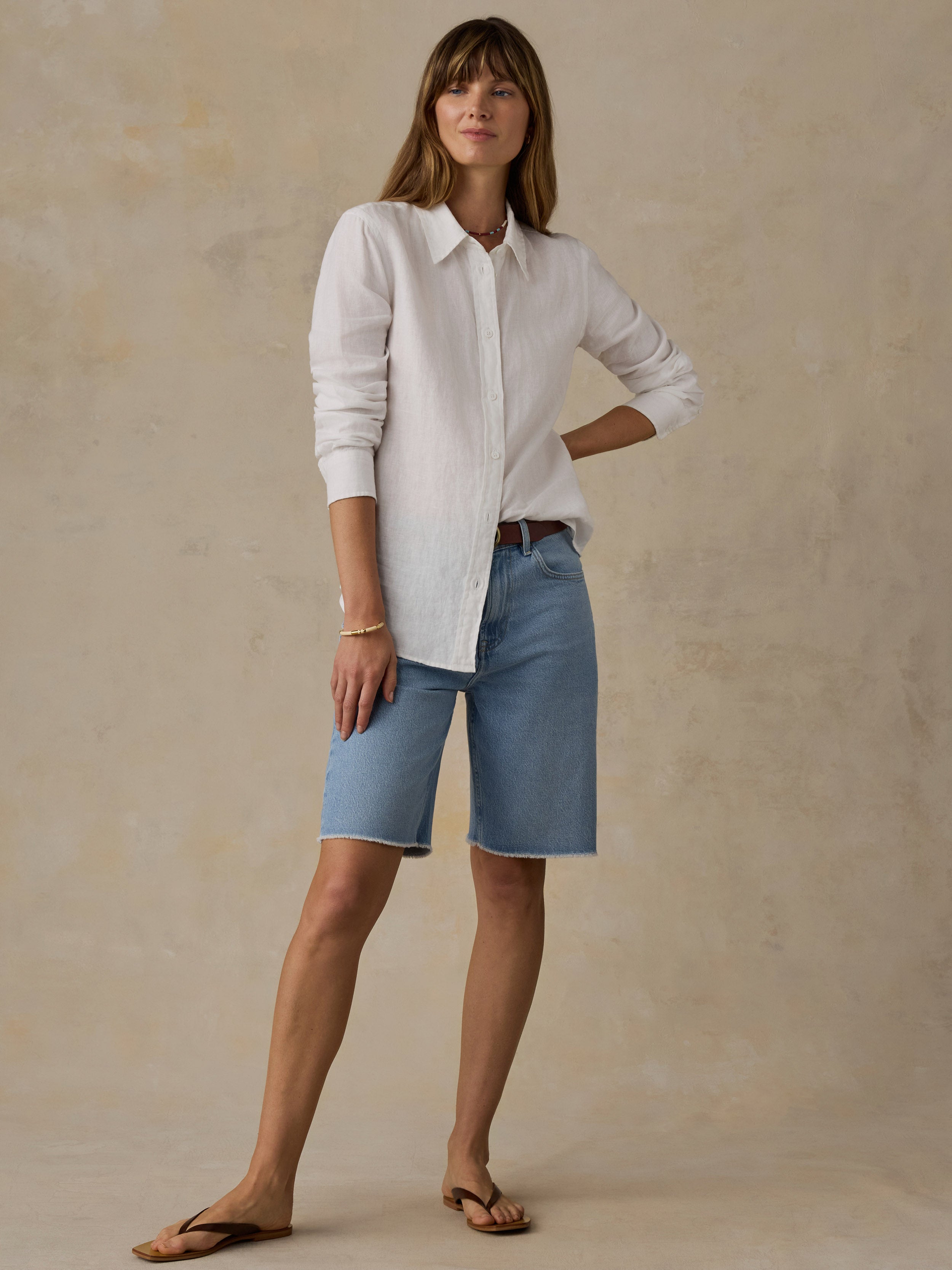 Woman wearing a white linen shirt and blue jean shorts against a beige background
