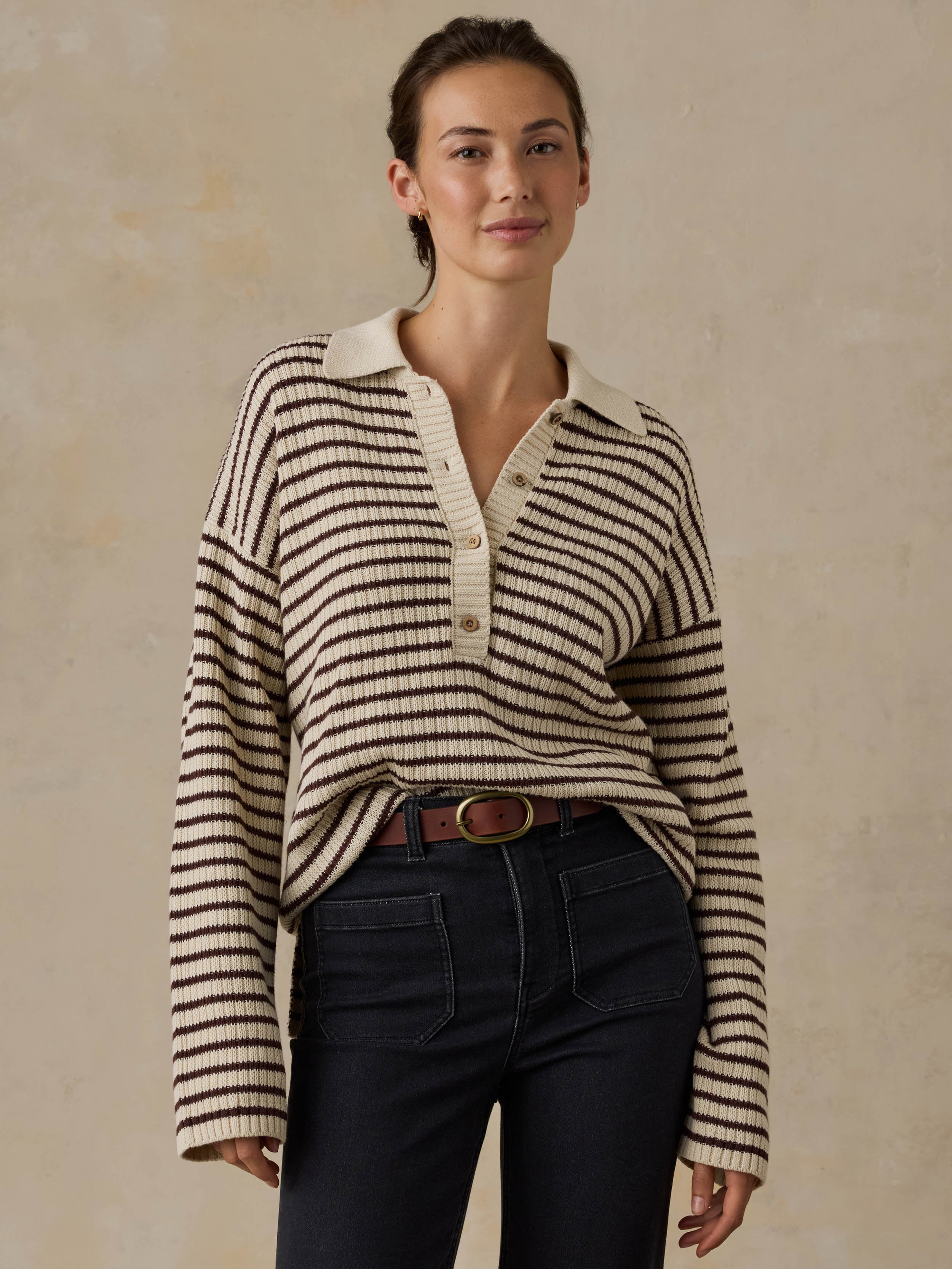 Woman wearing a striped sweater and black pants against a beige background