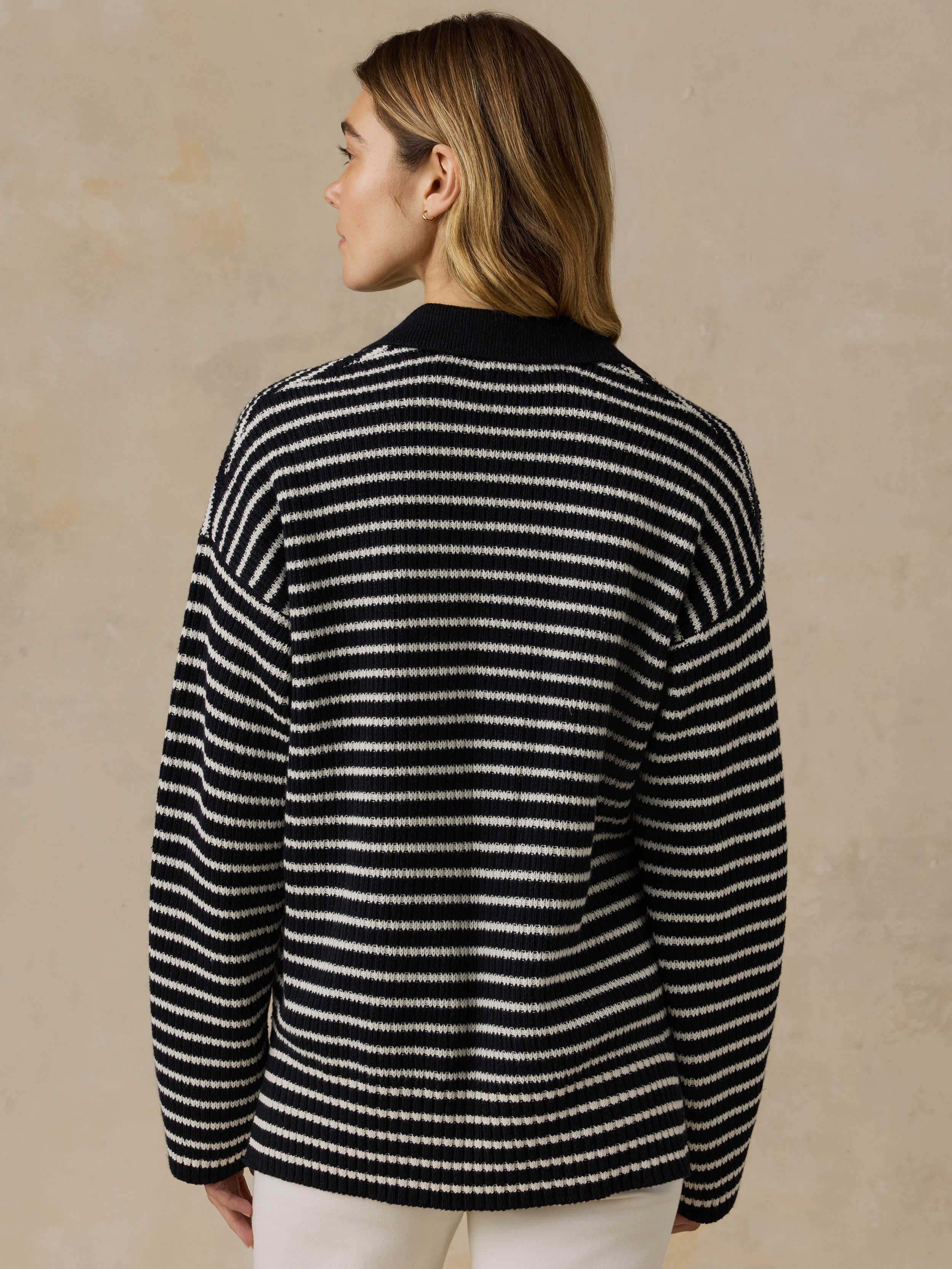 Woman wearing a blue and white striped sweater and white pants against a beige background