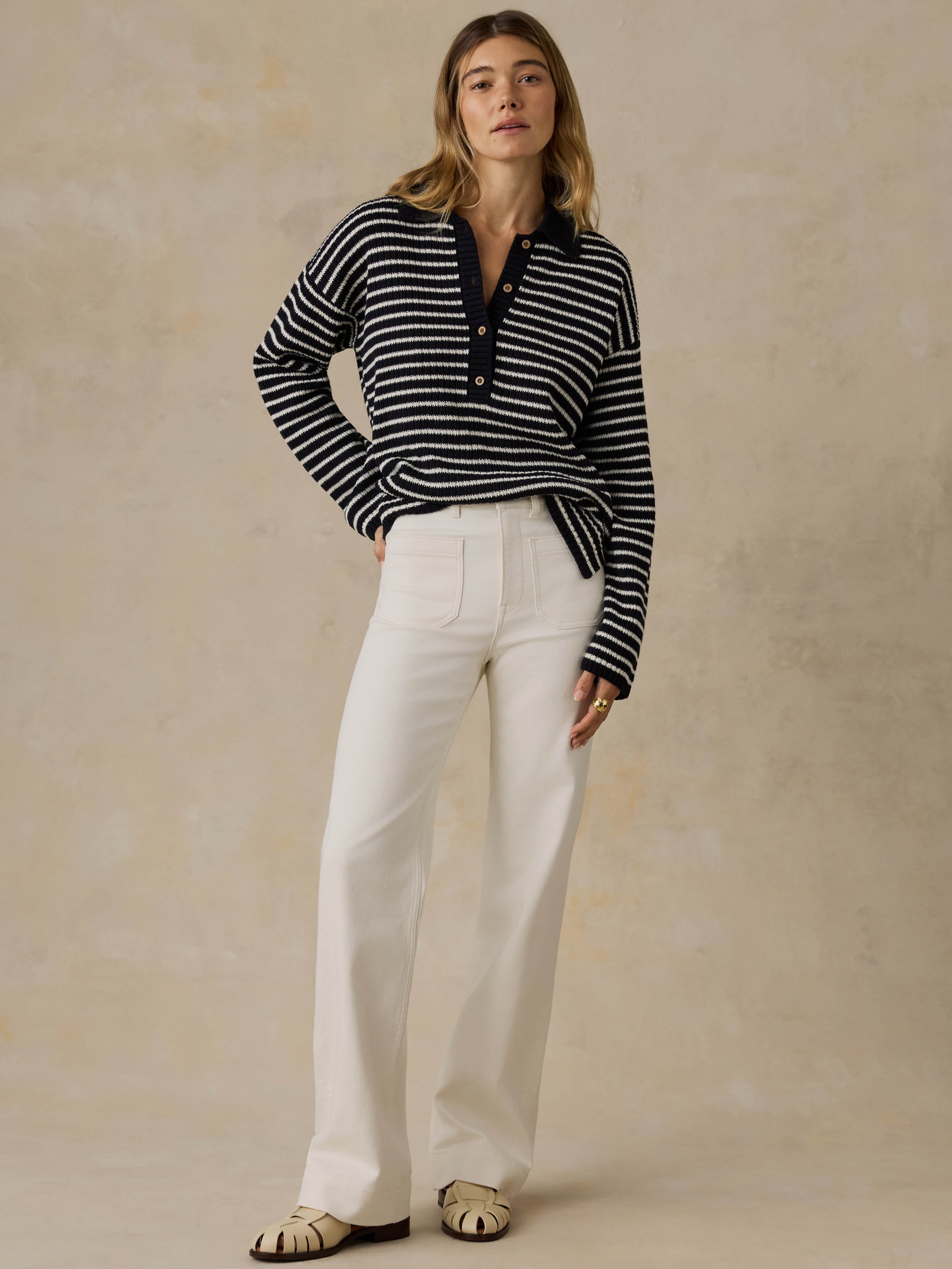 Woman wearing a blue and white striped sweater and white pants against a beige background