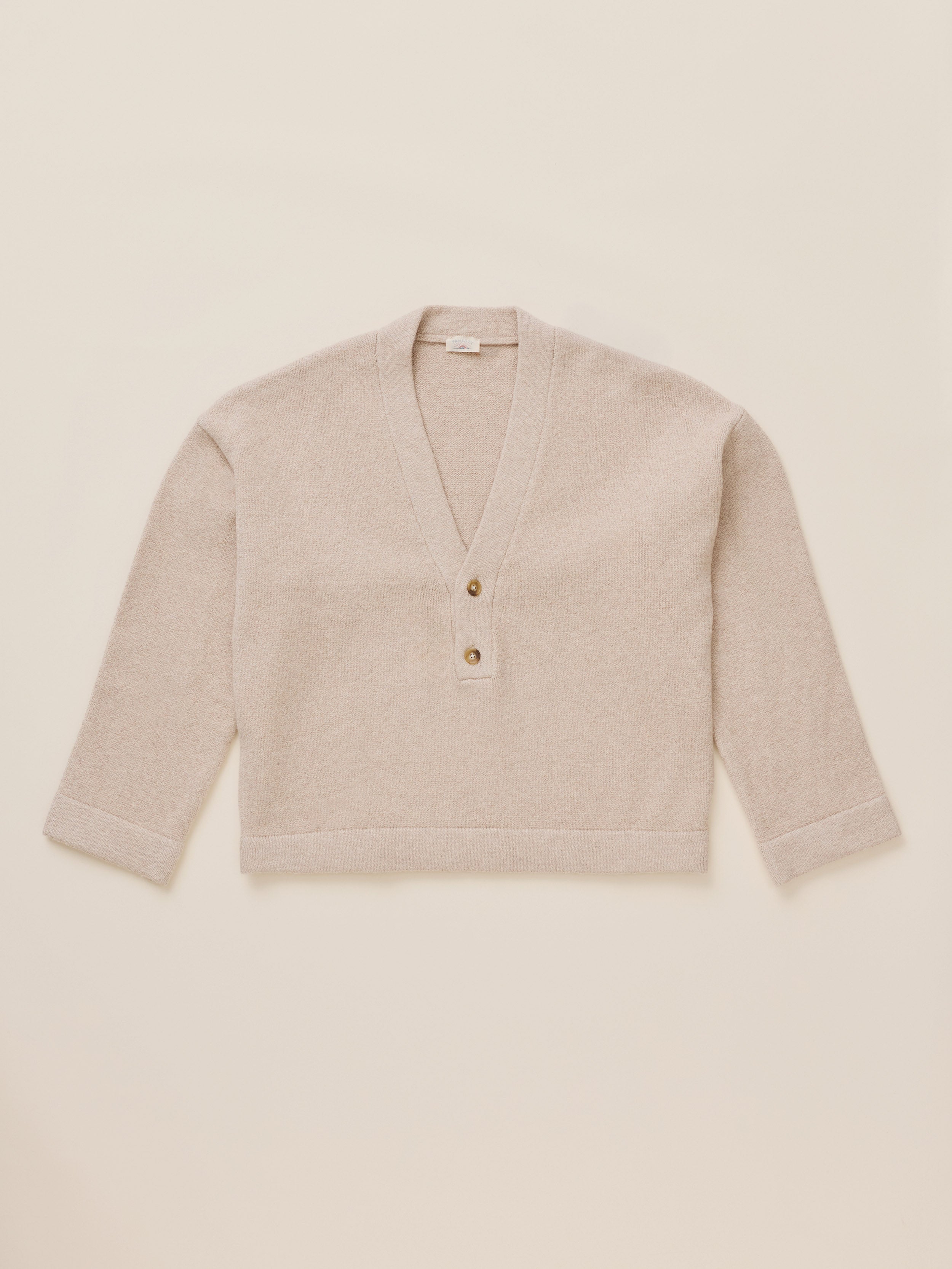 A light beige knit cardigan with a V-neck and three-quarter sleeves, featuring a three-button henley-style front, laid flat against a solid cream background.